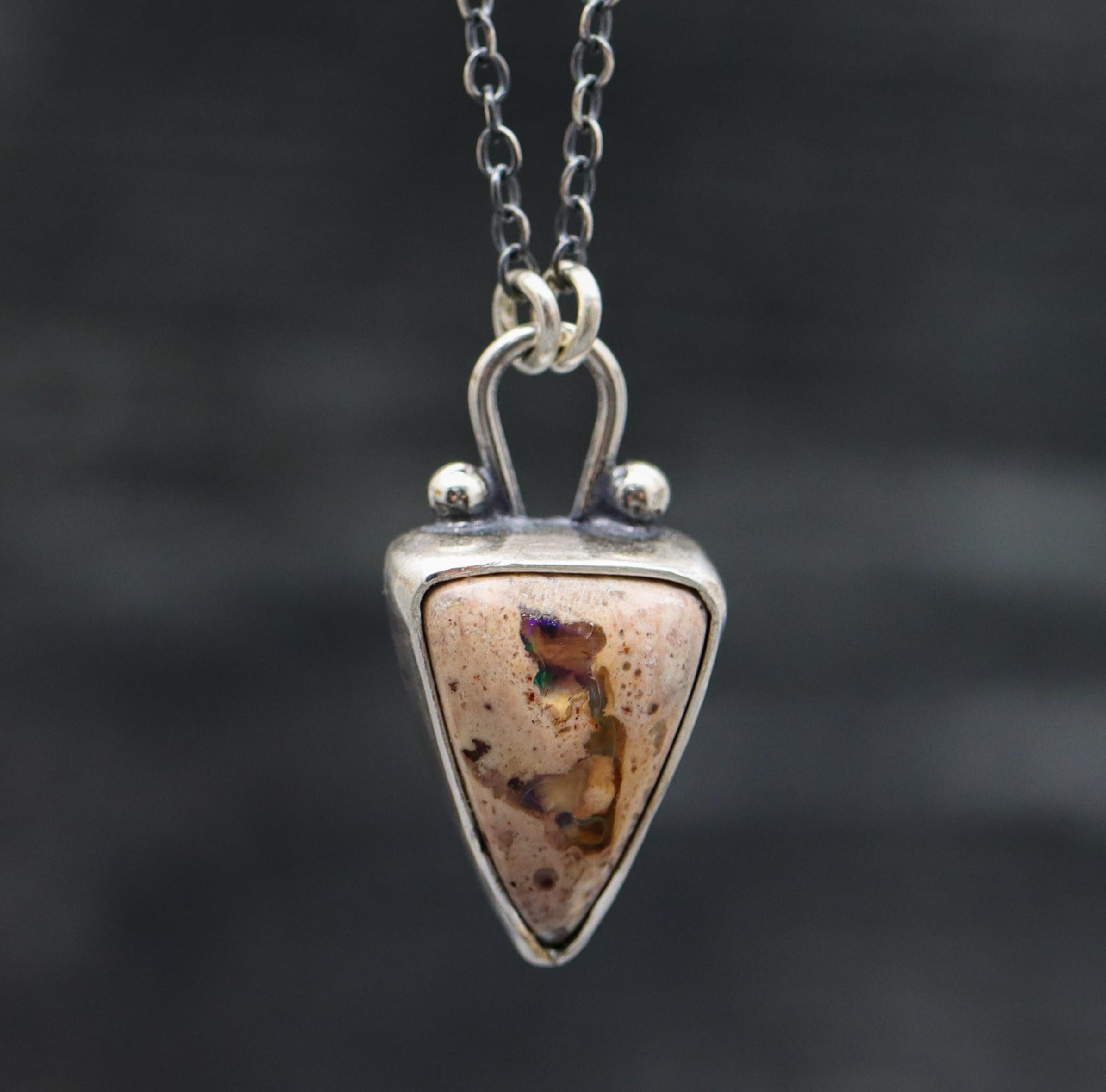 A sterling silver pendant necklace with a Mexican fire opal centerpiece and small silver ball accents, displayed against a dark background.