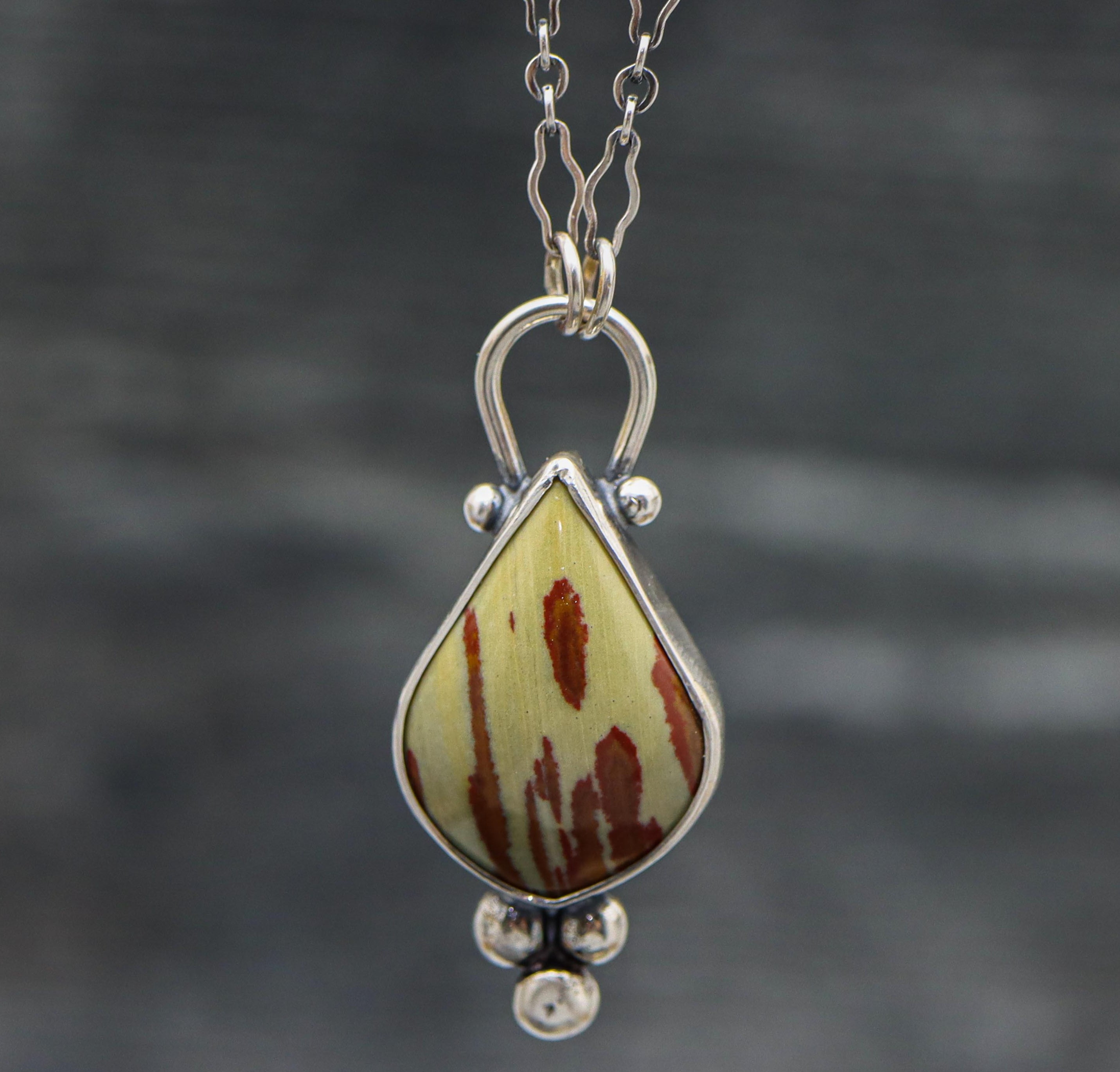 A sterling silver pendant featuring an owyhee jasper gemstone with a textured metal surface mimicking the stone's pattern, displayed on a silver chain.