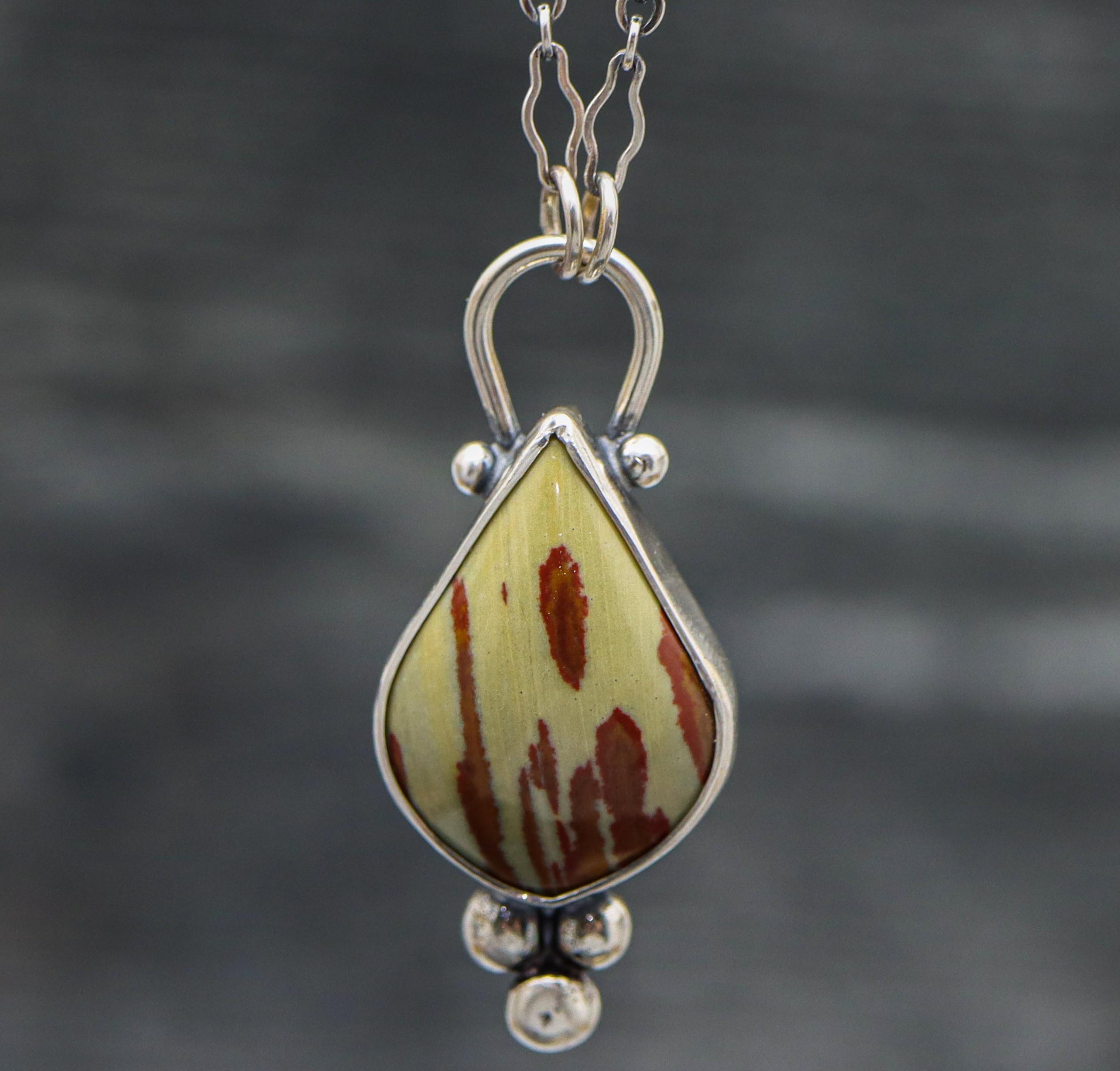 A sterling silver pendant featuring an owyhee jasper gemstone with a textured metal surface mimicking the stone's pattern, displayed on a silver chain.