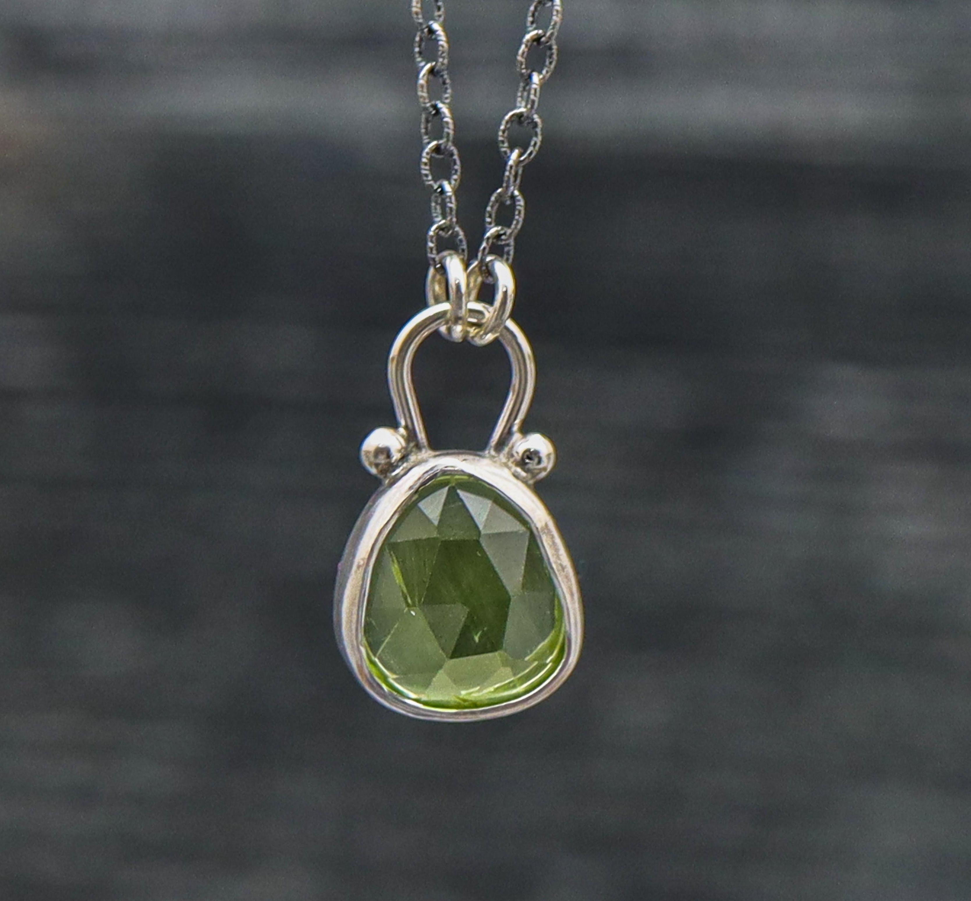A sterling silver pendant necklace with a faceted rose cut green peridot centerpiece, suspended from a silver chain.