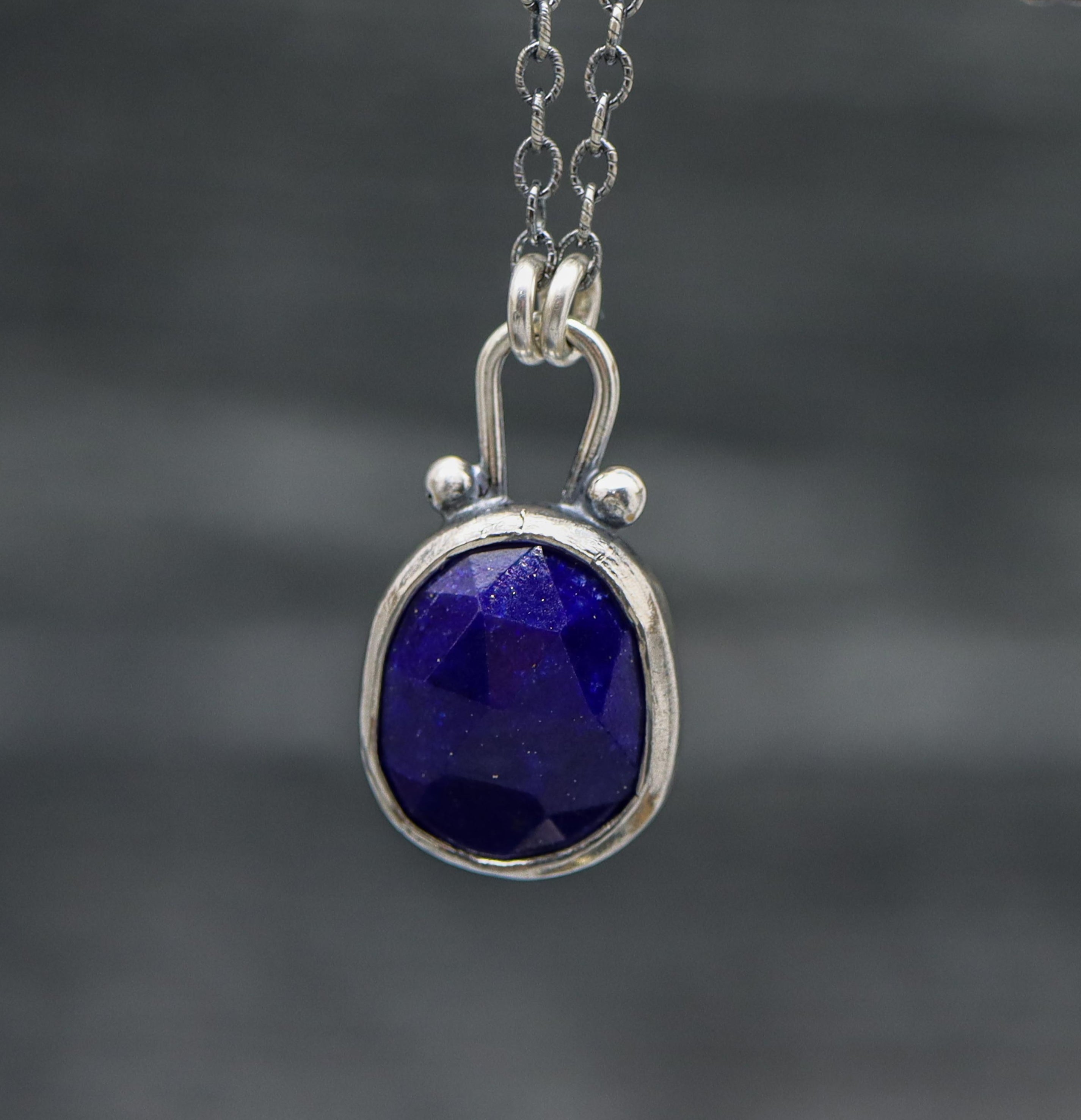 Silver pendant with a blue lapis gemstone on a chain against a dark background