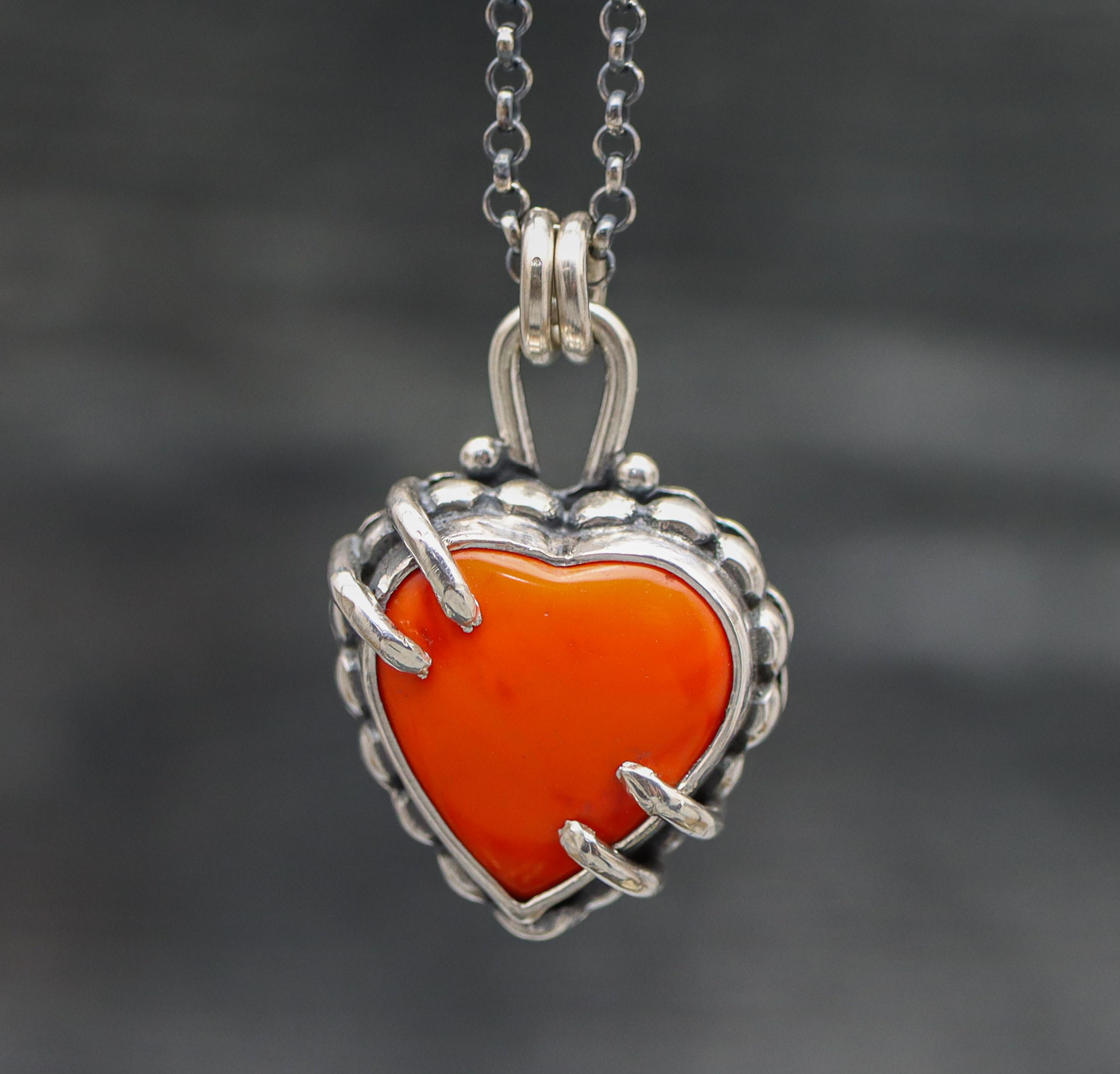 A red rosarita heart-shaped pendant necklace with a sterling silver setting, suspended from a silver rolo chain.