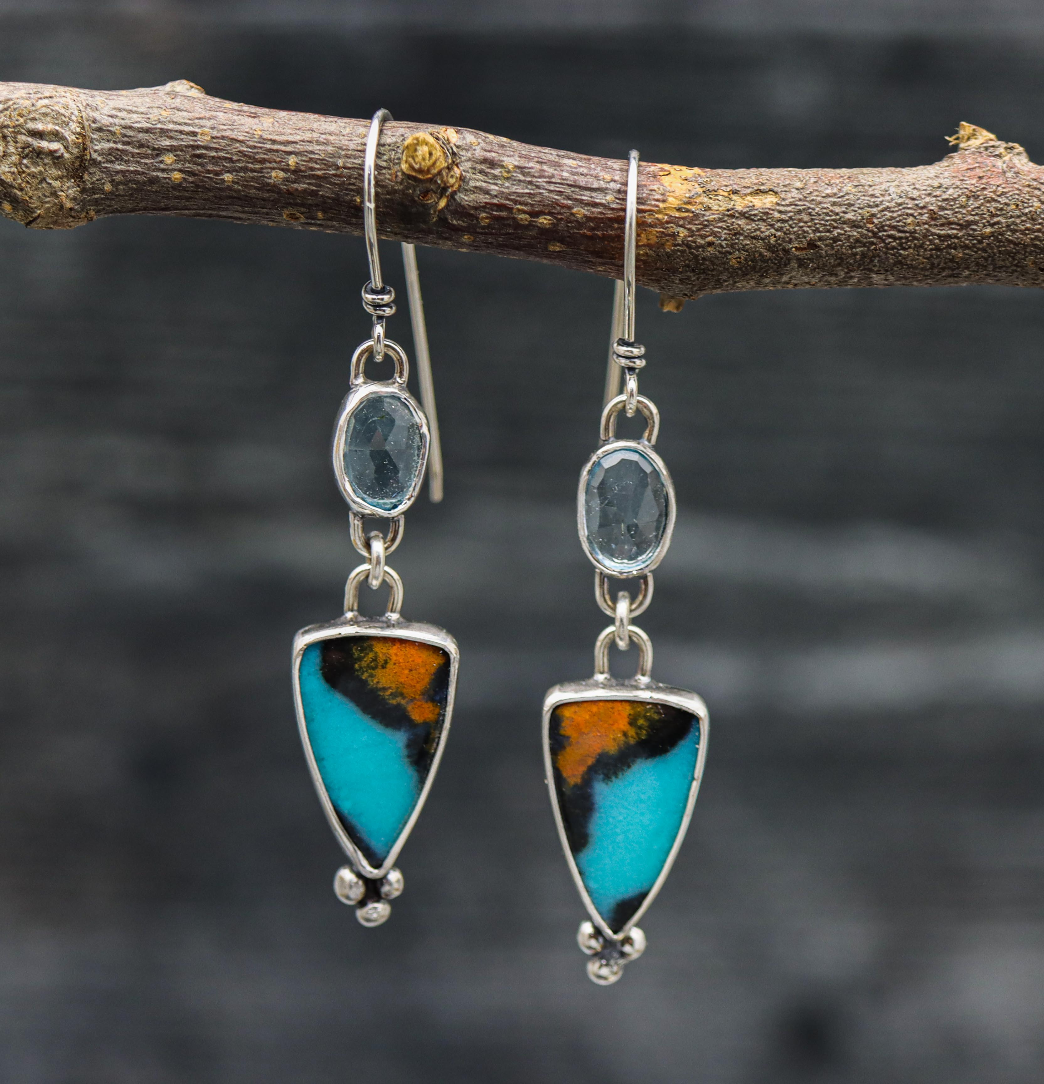 A pair of sterling silver dangle earrings with chrysocolla stones and blue topaz accents, displayed against a natural outdoor background.