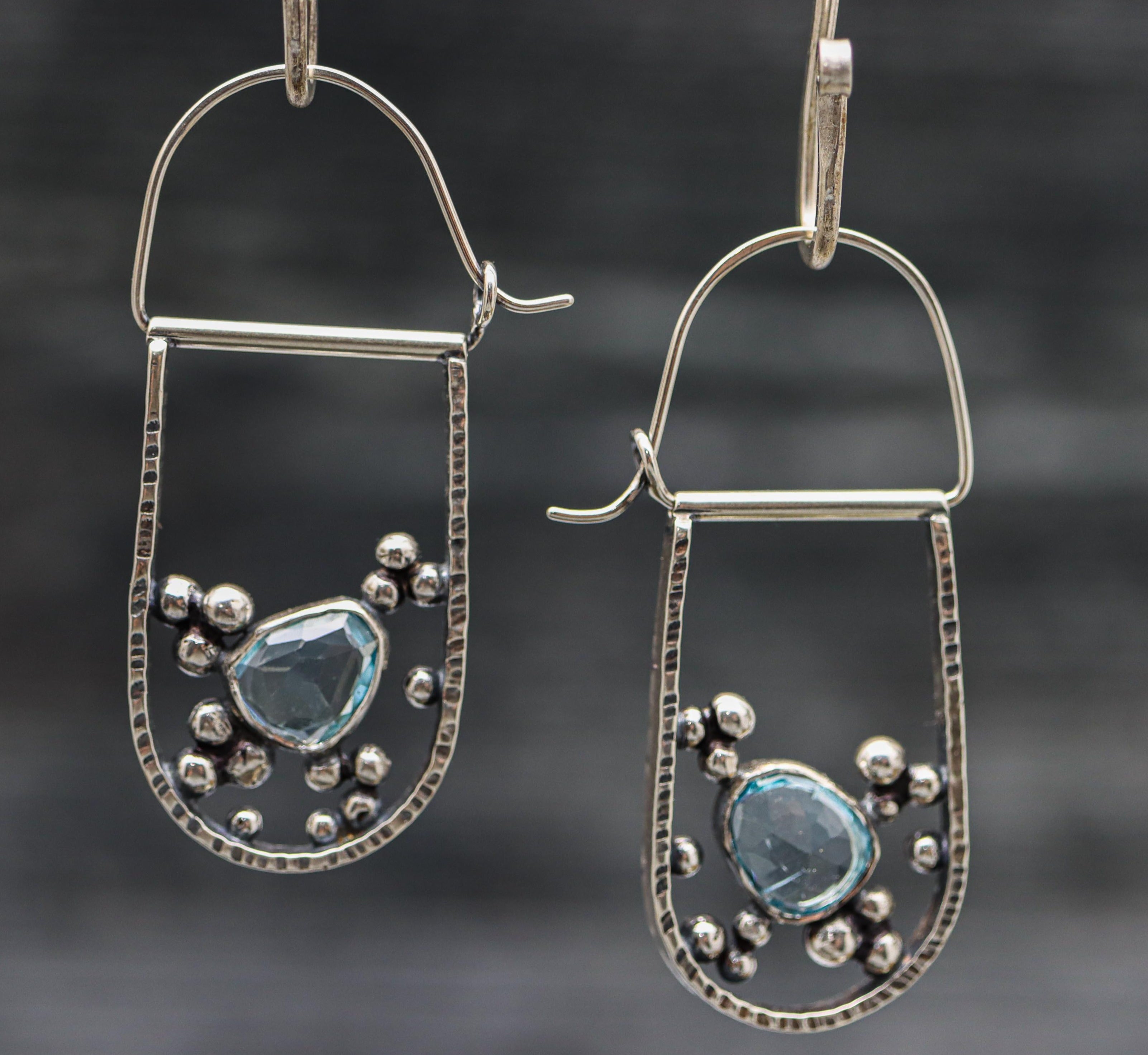 A pair of sterling silver hoop earrings with blue topaz accents and small silver beads.
