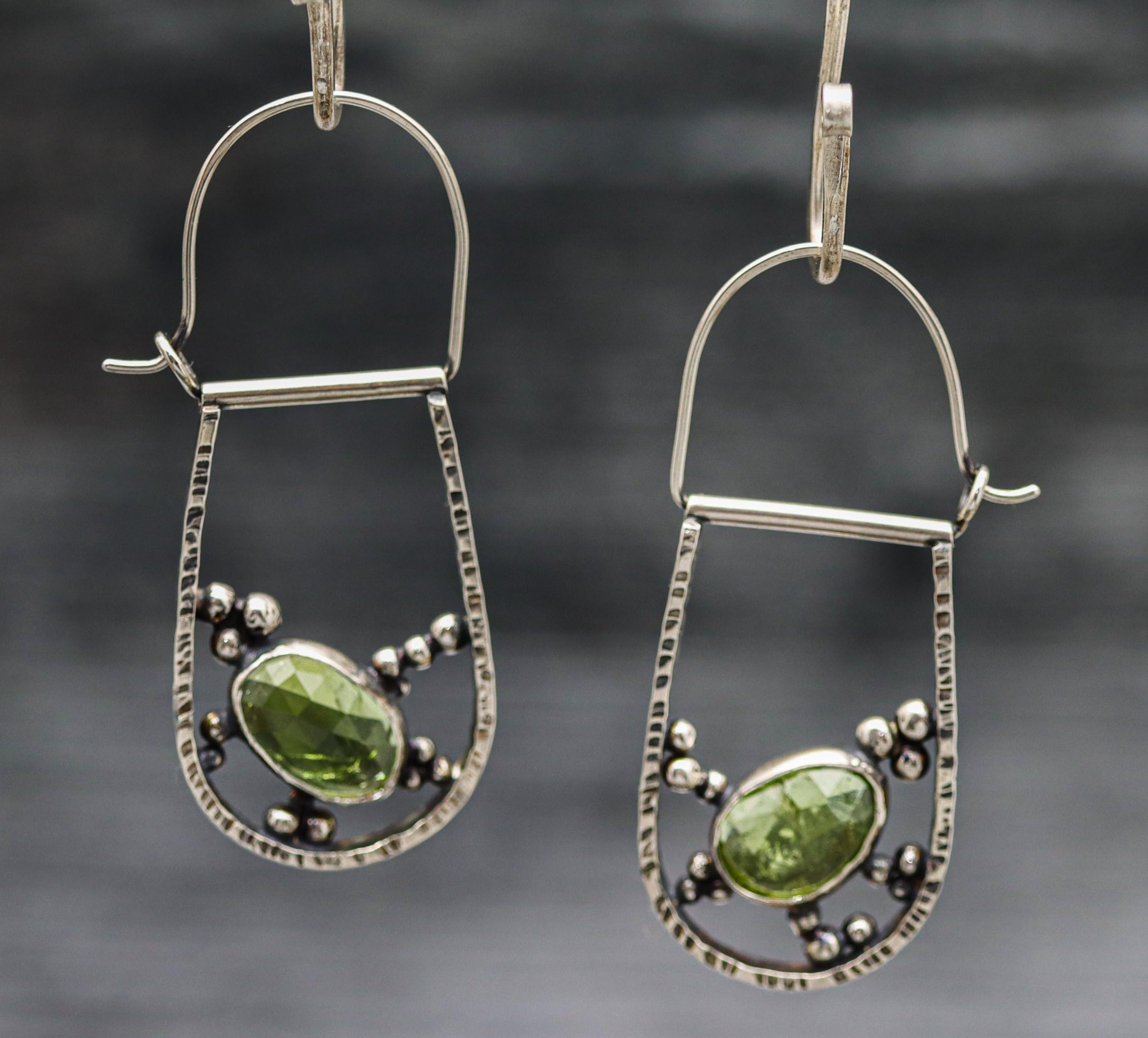 A pair of sterling silver hoop earrings with green tourmaline and silver accents.