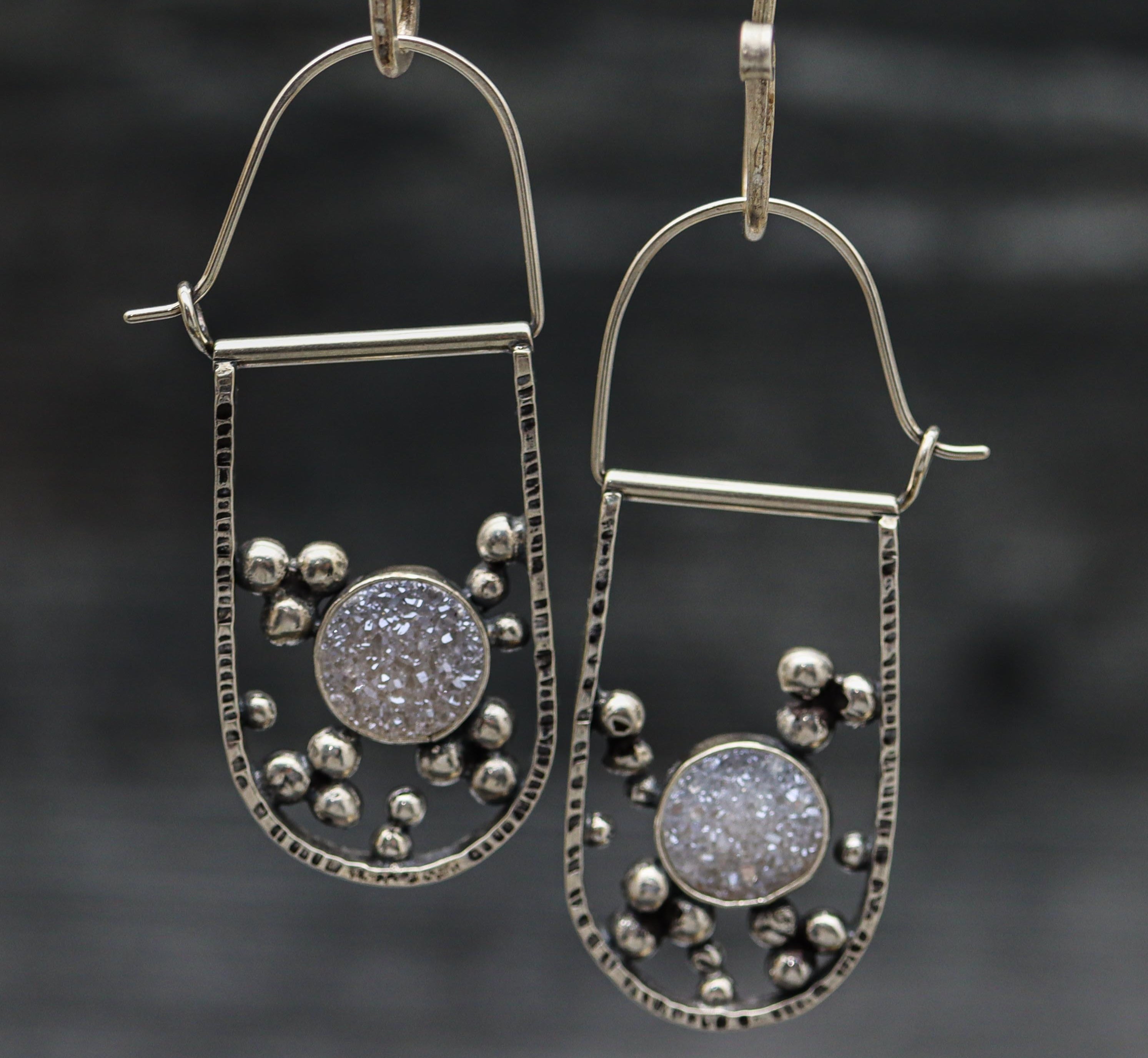 A pair of sterling silver hoop earrings with white druzy u-shaped design displayed against a dark background.