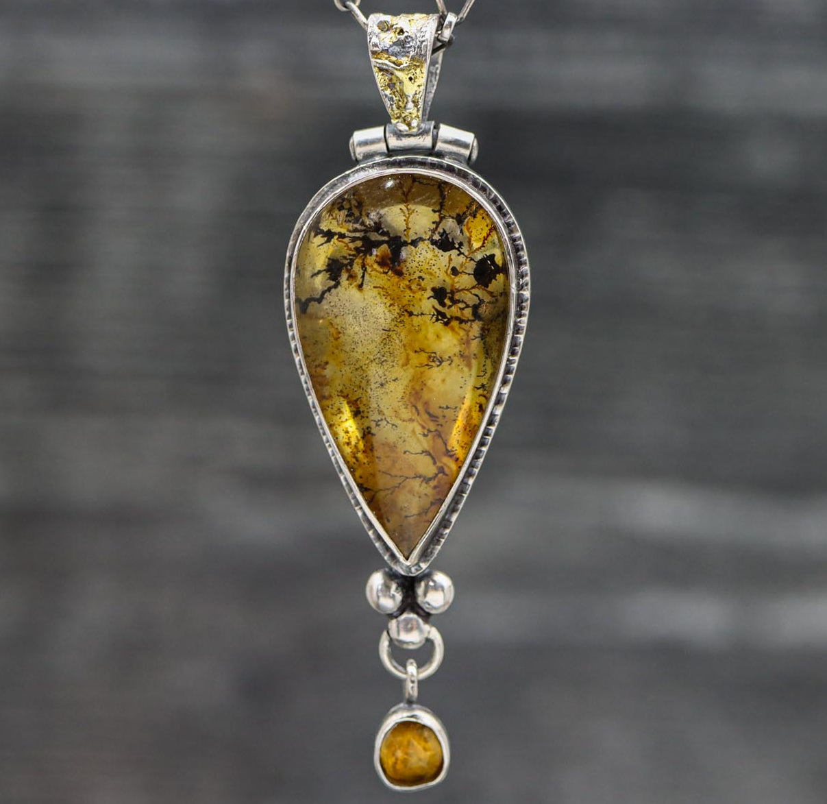 A sterling silver pendant featuring a dendritic quartz with iron staining and a faceted rose cut mandarine citrine below, with a textured bail and gold accents.