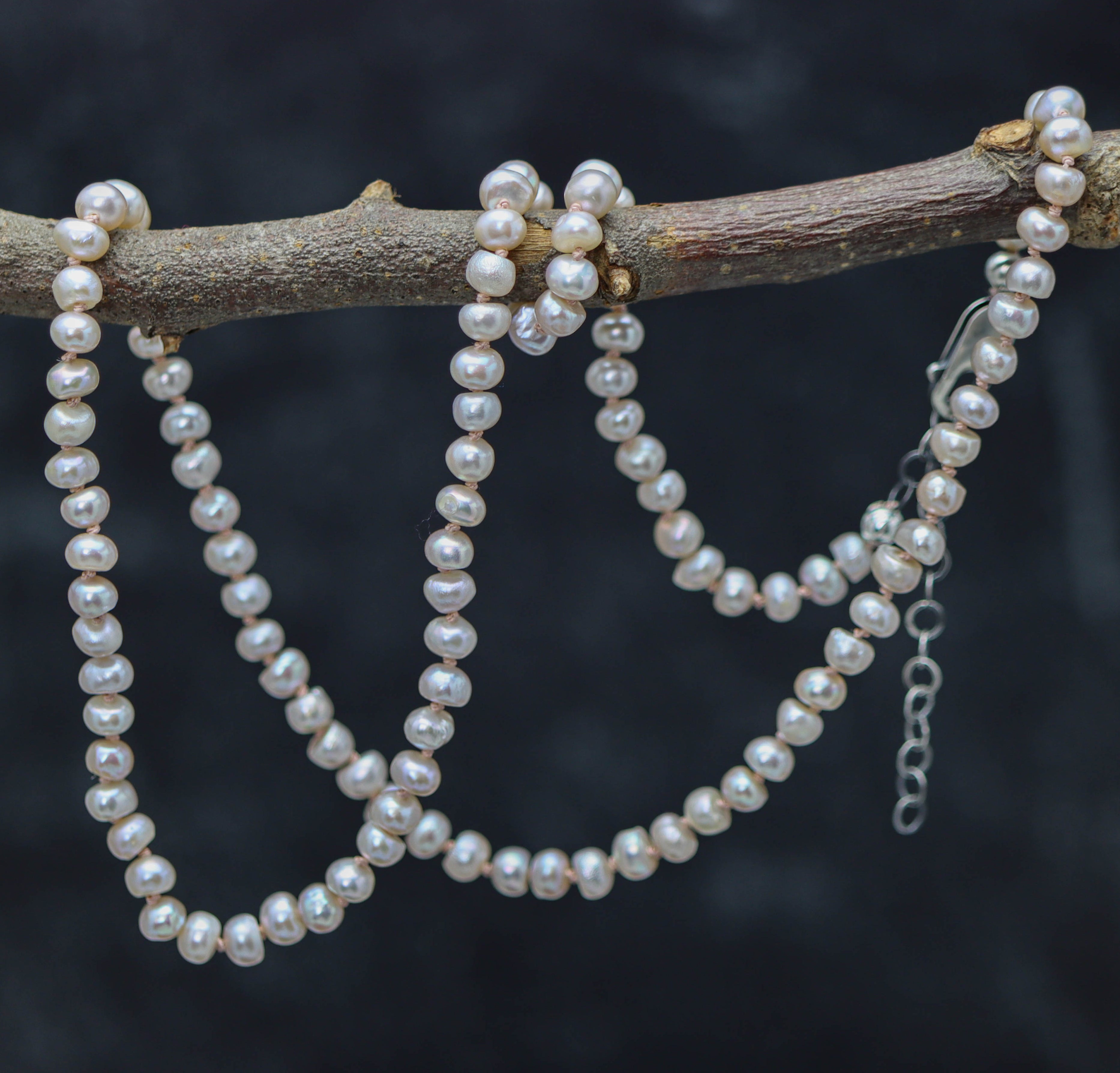 A sterling silver necklace featuring hand knotted strands of light pink pearl beads, with a lobster claw closure and an extension chain.