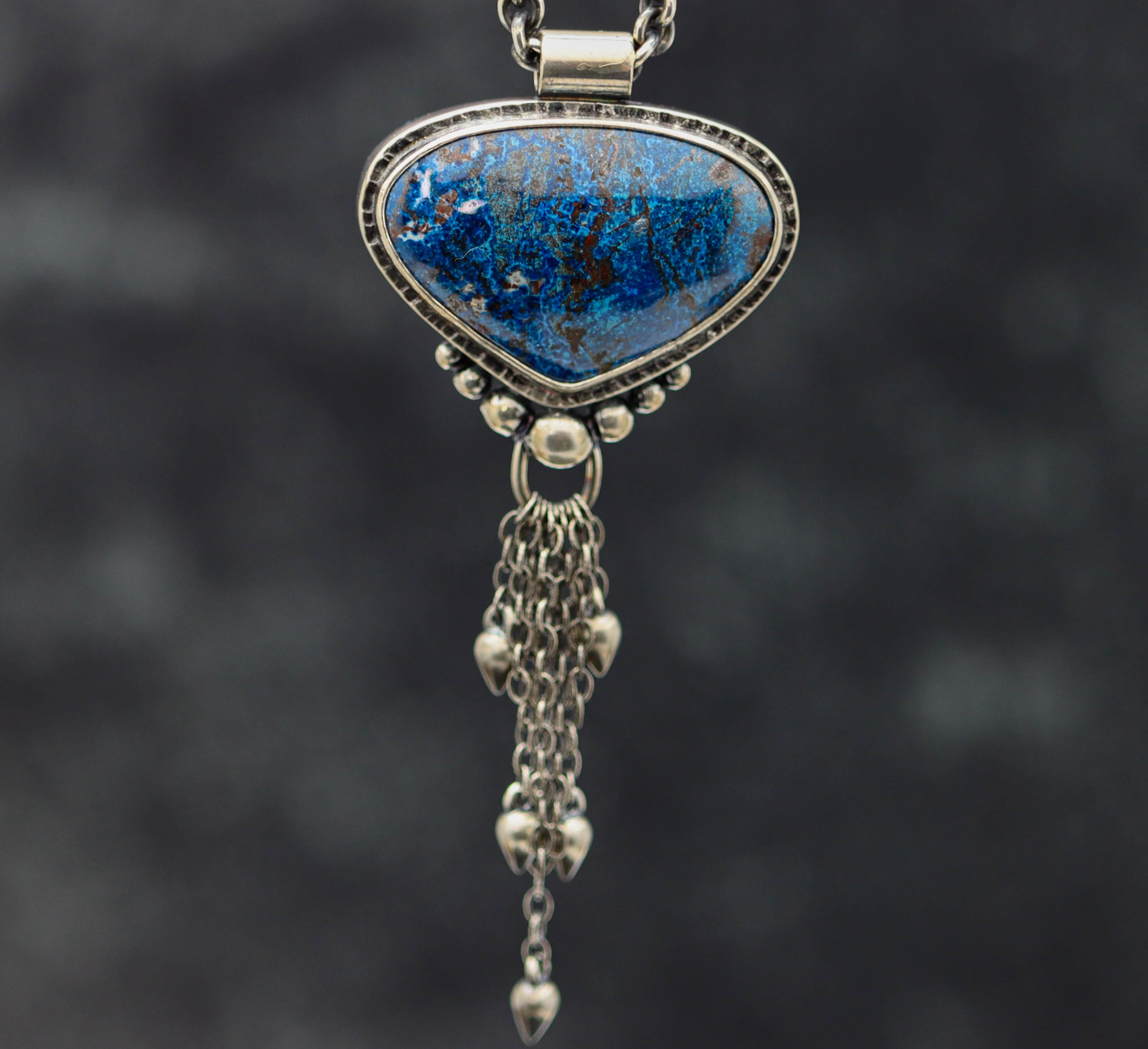 A sterling silver pendant featuring a blue shattuckite gemstone, suspended by a silver chain with a tassel.