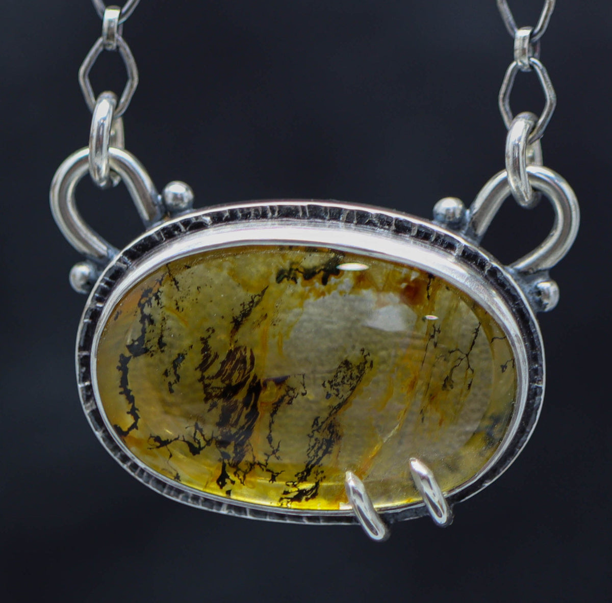 A dendritic quartz pendant set in a sterling silver double bezel pendant with a lobster claw closure on a chain.