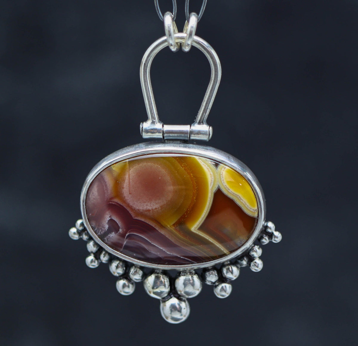 A sterling silver pendant featuring an Agua Nueva agate gemstone, with silver ball details and a ruffled silver bail, suspended by a silver chain.