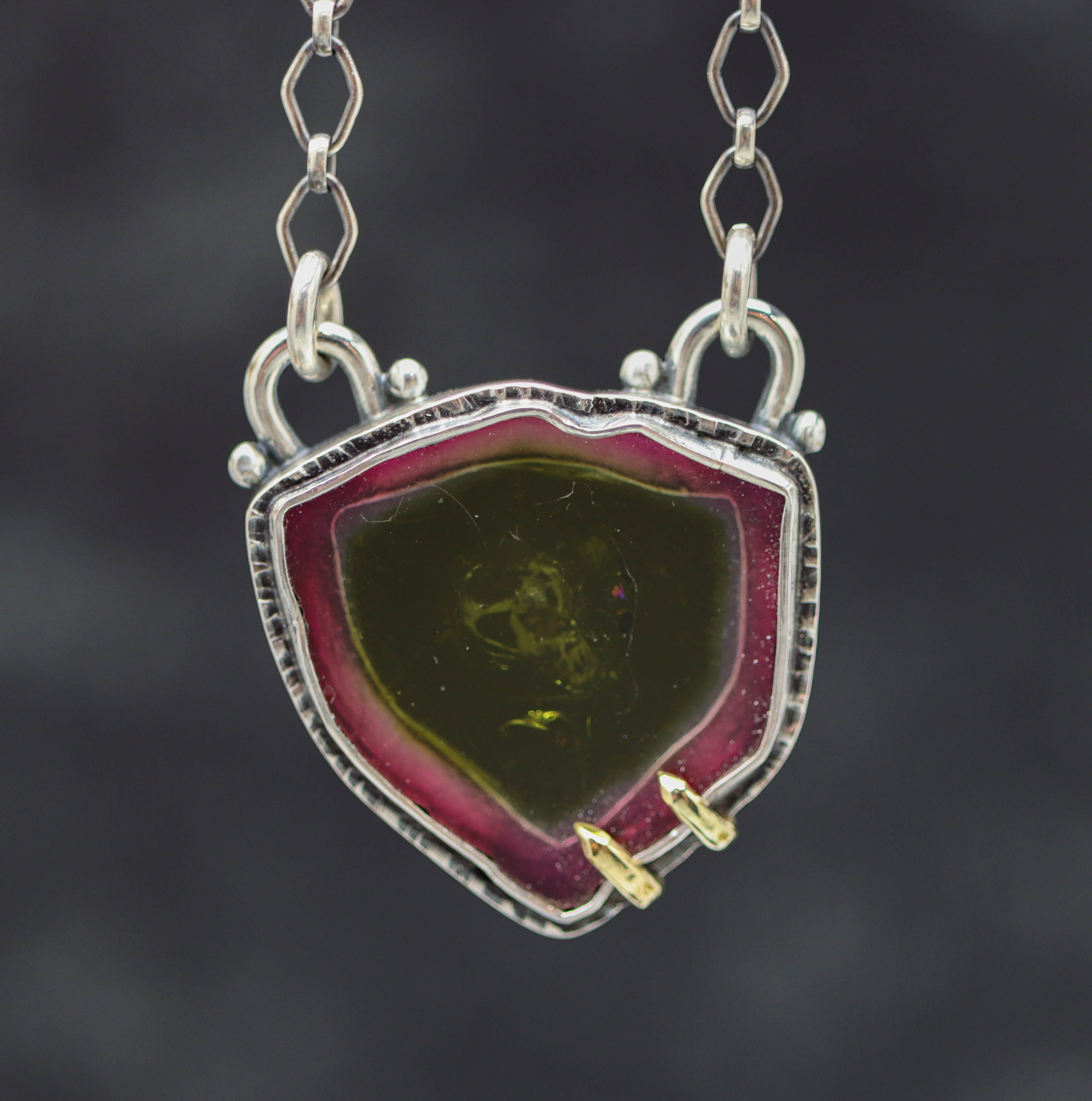 A watermelon tourmaline slice pendant necklace with a silver and gold bezel, on a textured link chain.