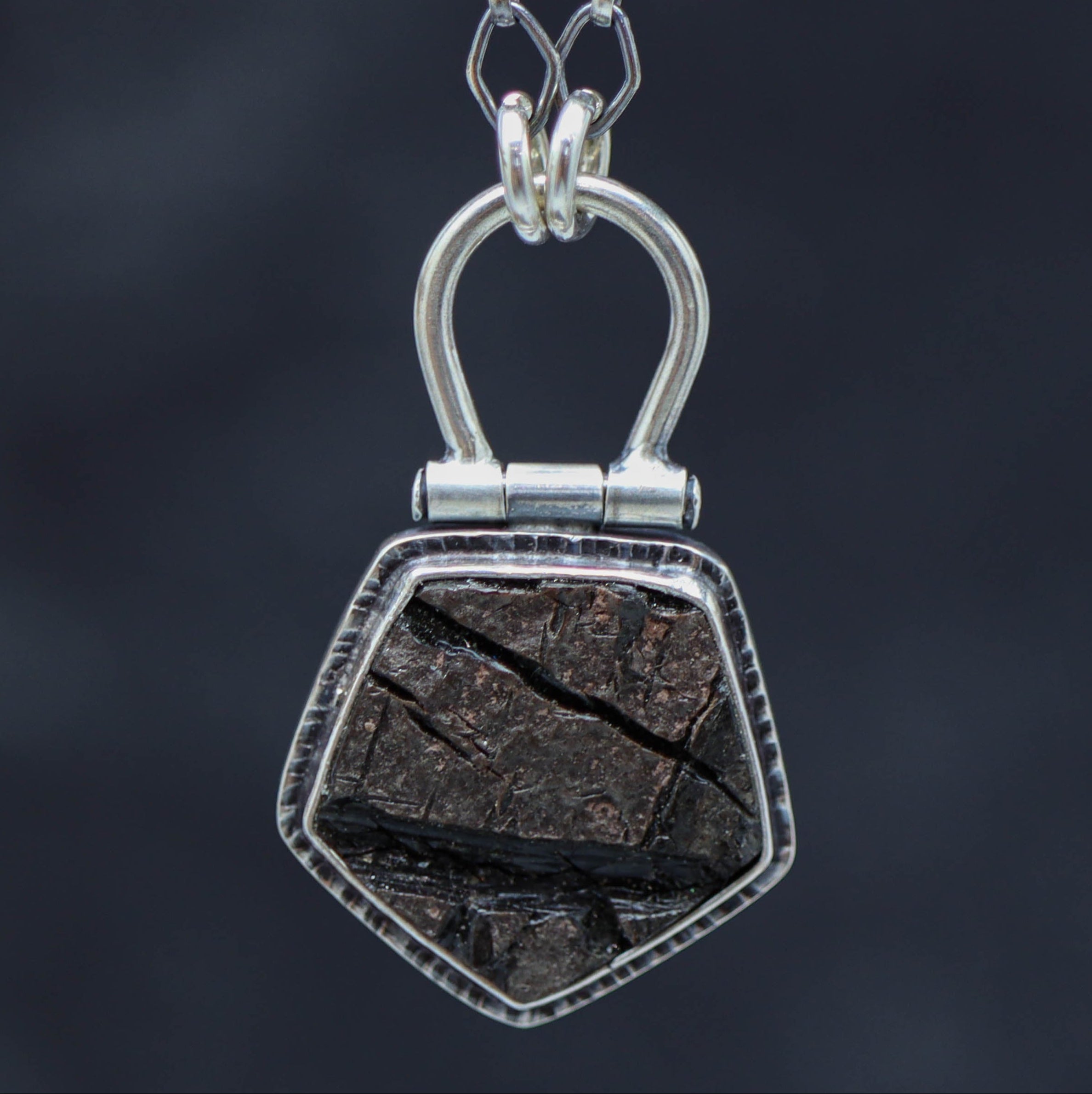 A sterling silver necklace with a natural surface obsidian pendant, displayed on a tree branch.