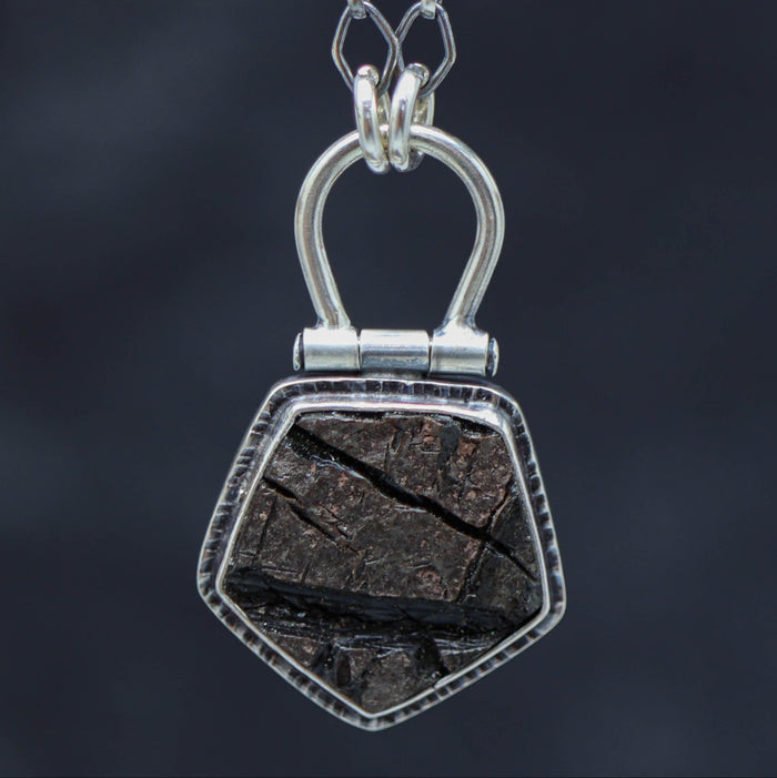 A sterling silver necklace with a natural surface obsidian pendant, displayed on a tree branch.