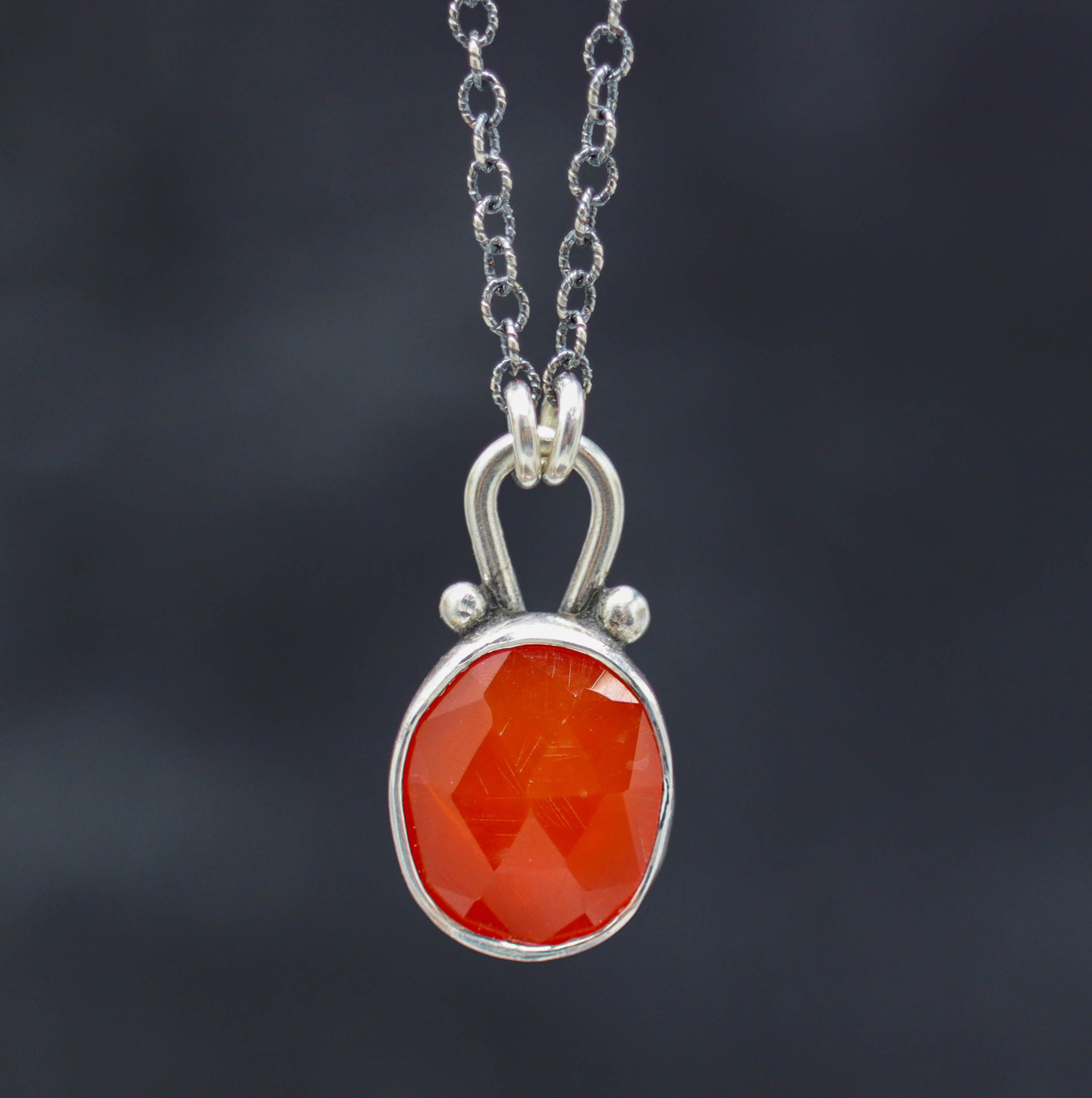 A sterling silver pendant necklace with a juicy bright orange carnelian gemstone in a faceted rose cut, suspended by a silver ball and a lobster claw closure.