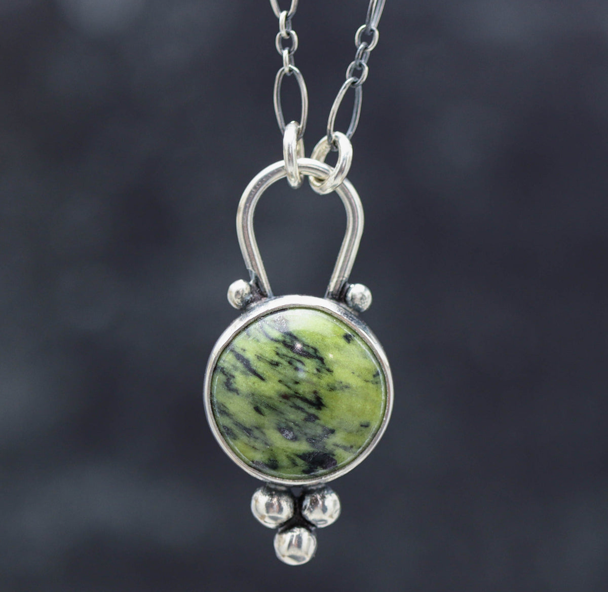 A green serpentine pendant with a sterling silver metal setting, attached to a silver chain.