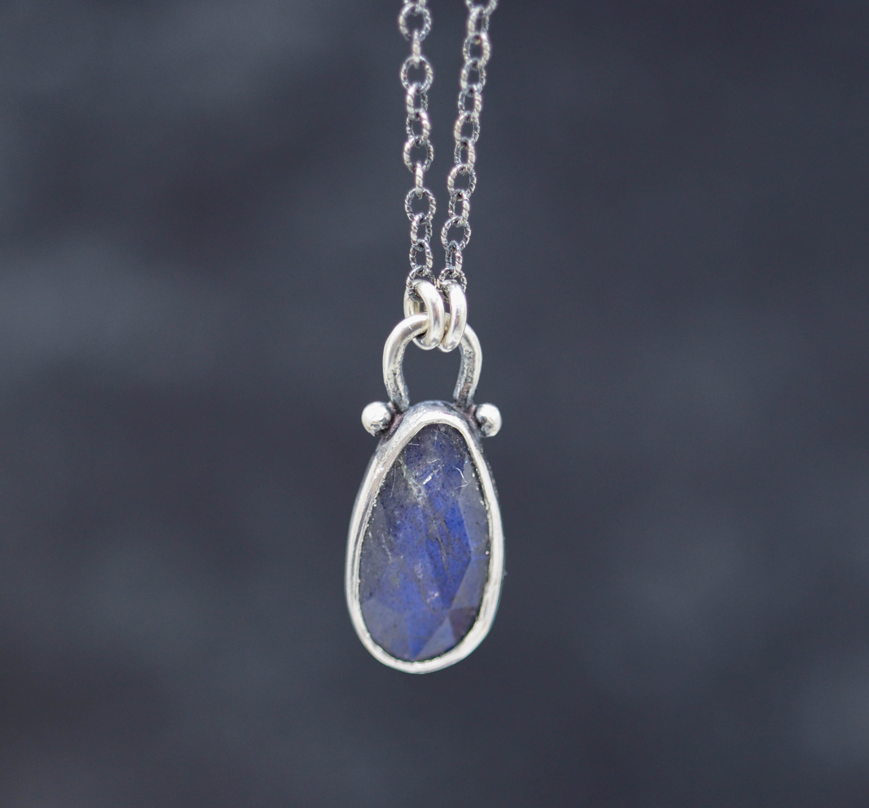 A sterling silver pendant necklace with a faceted rose cut labradorite gemstone, displayed against a blurred background.