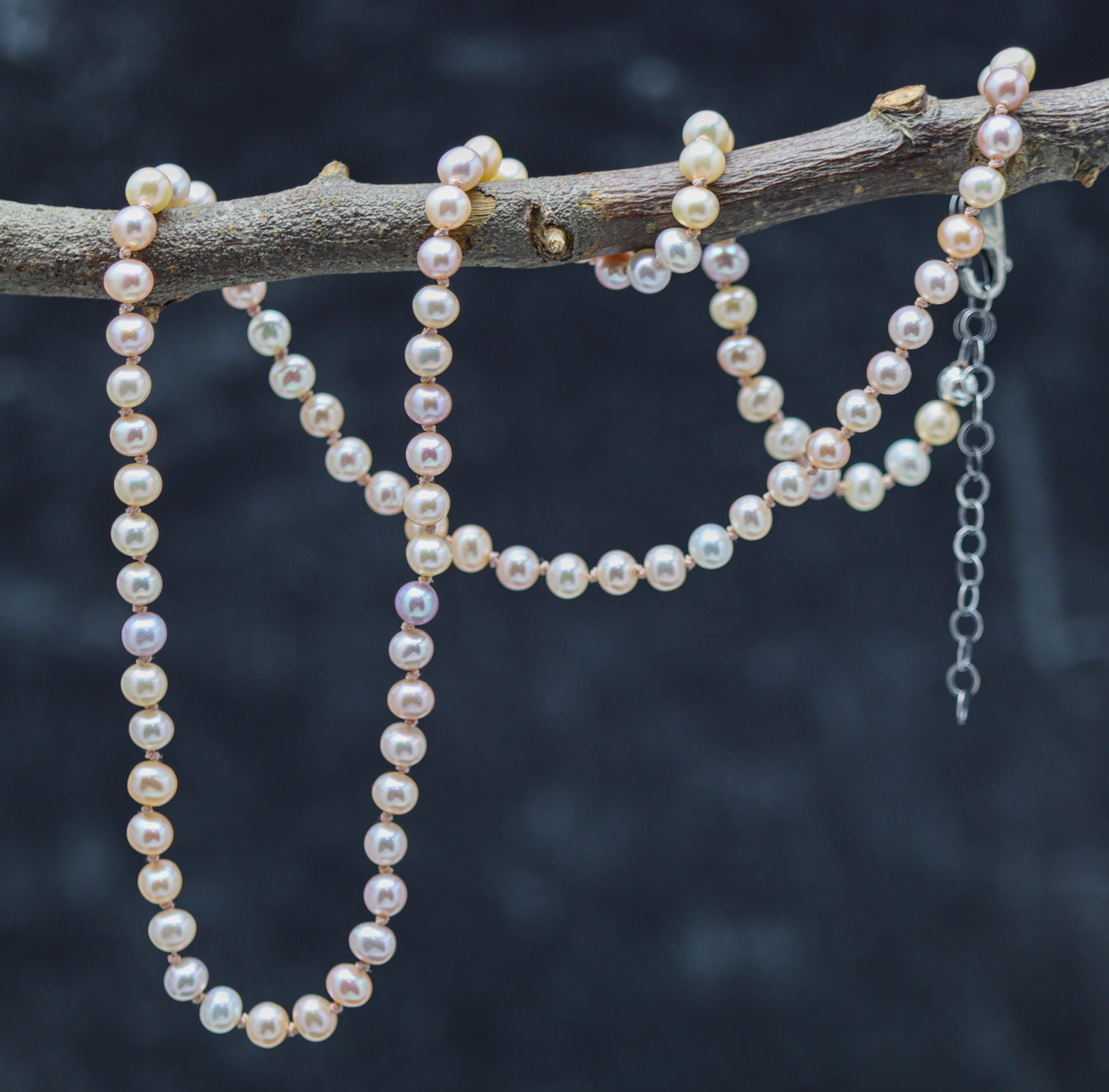 A sterling silver necklace featuring hand knotted strands of pink pearl beads, with a lobster claw closure, displayed against a dark background.