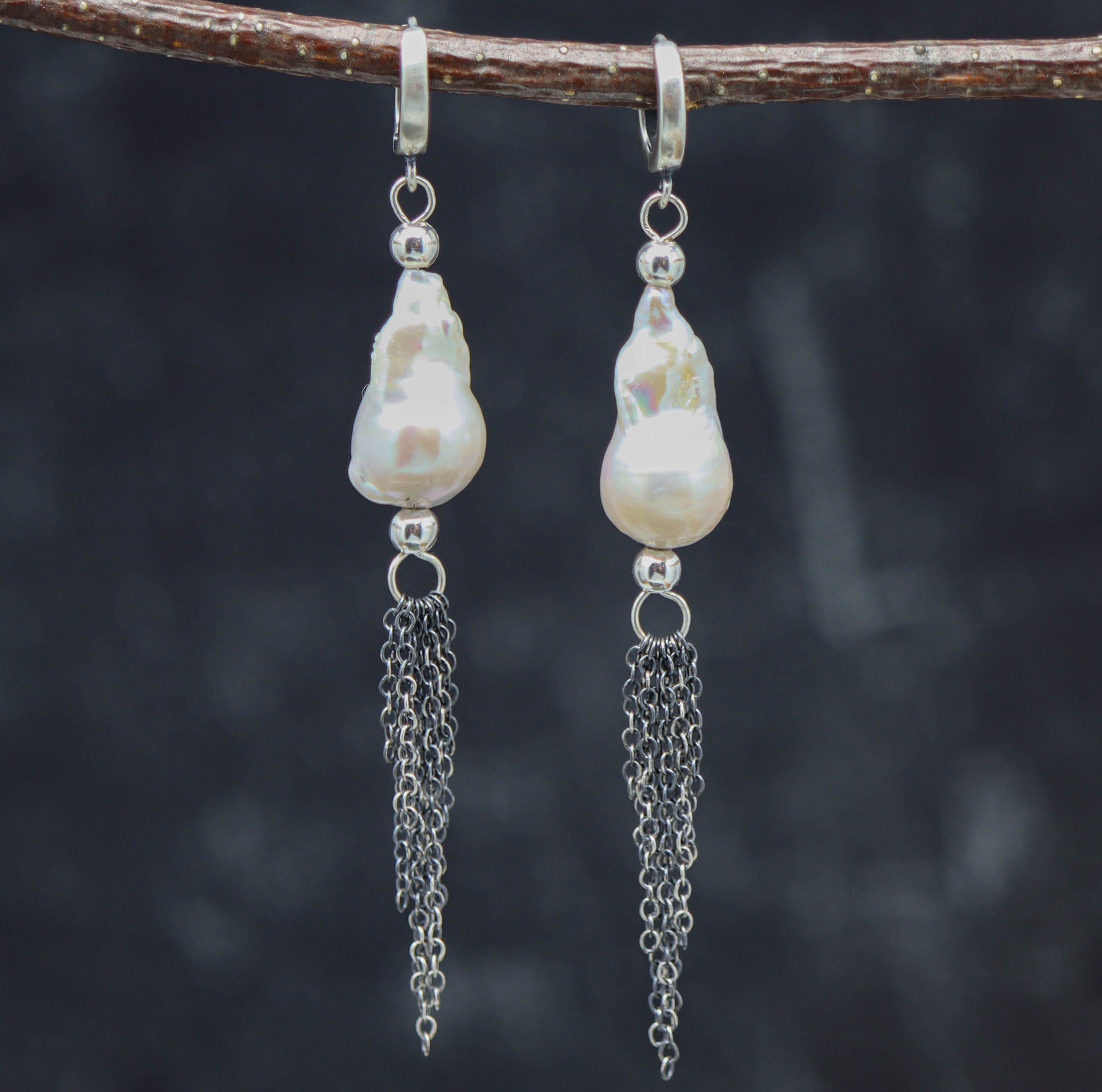 A pair of sterling silver baroque pearl dangle fringe earrings displayed on a branch against a dark background.