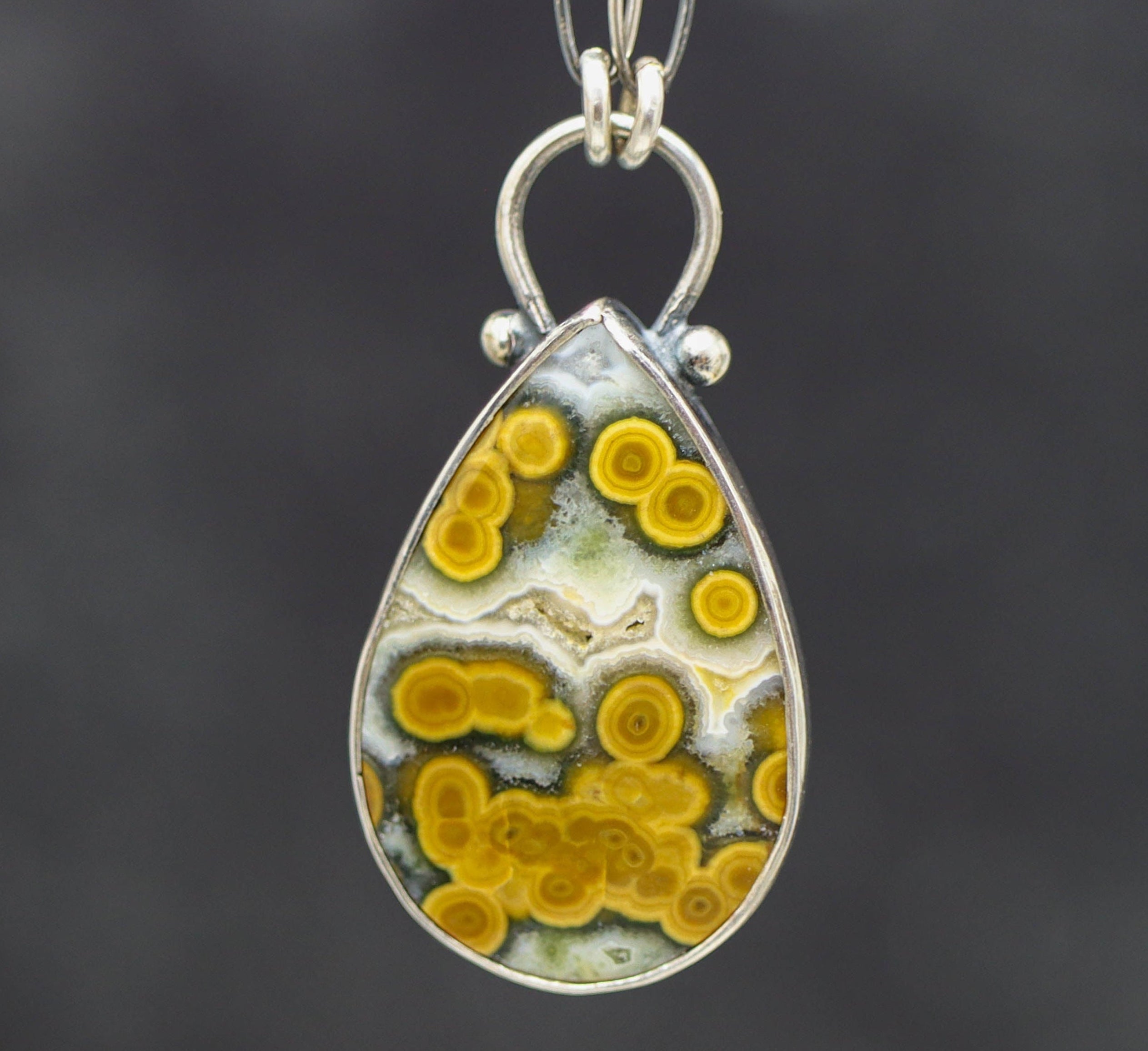 Teardrop-shaped pendant with yellow and white pattern on a dark background