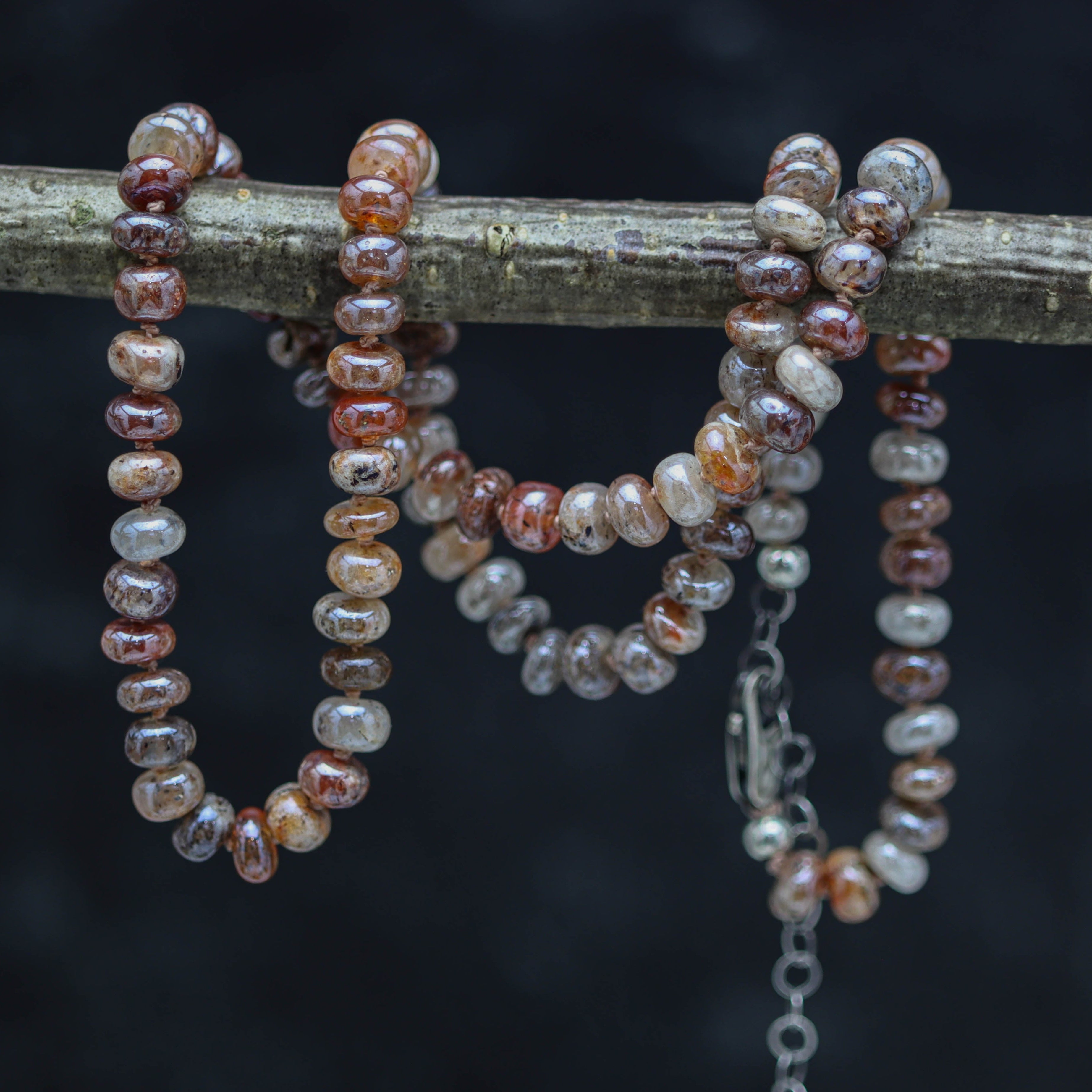 A hand knotted bead necklace with sterling silver and moonstone beads, displayed on a branch against a dark background.