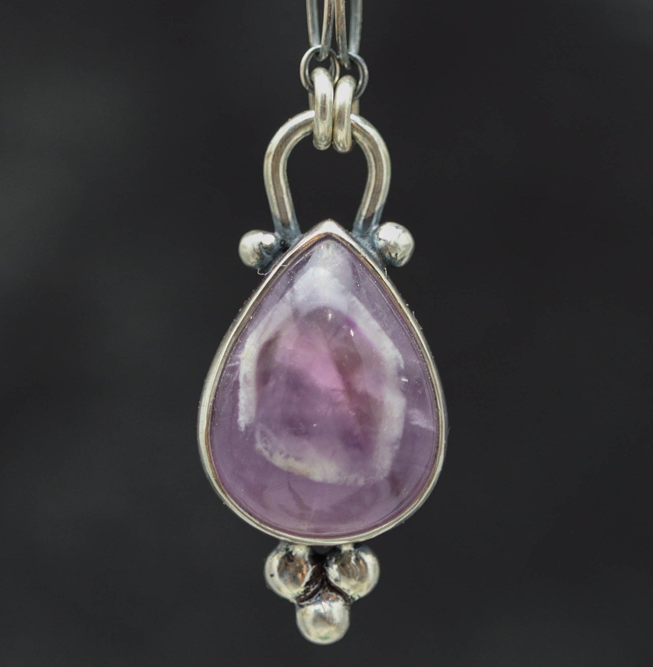 Teardrop-shaped purple gemstone pendant on a chain against a dark background