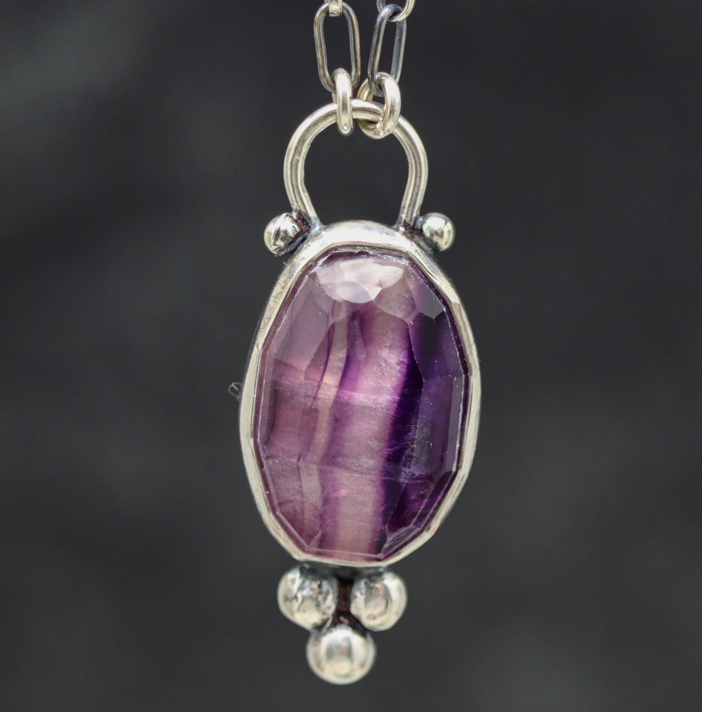 Silver pendant with a purple gemstone on a dark background