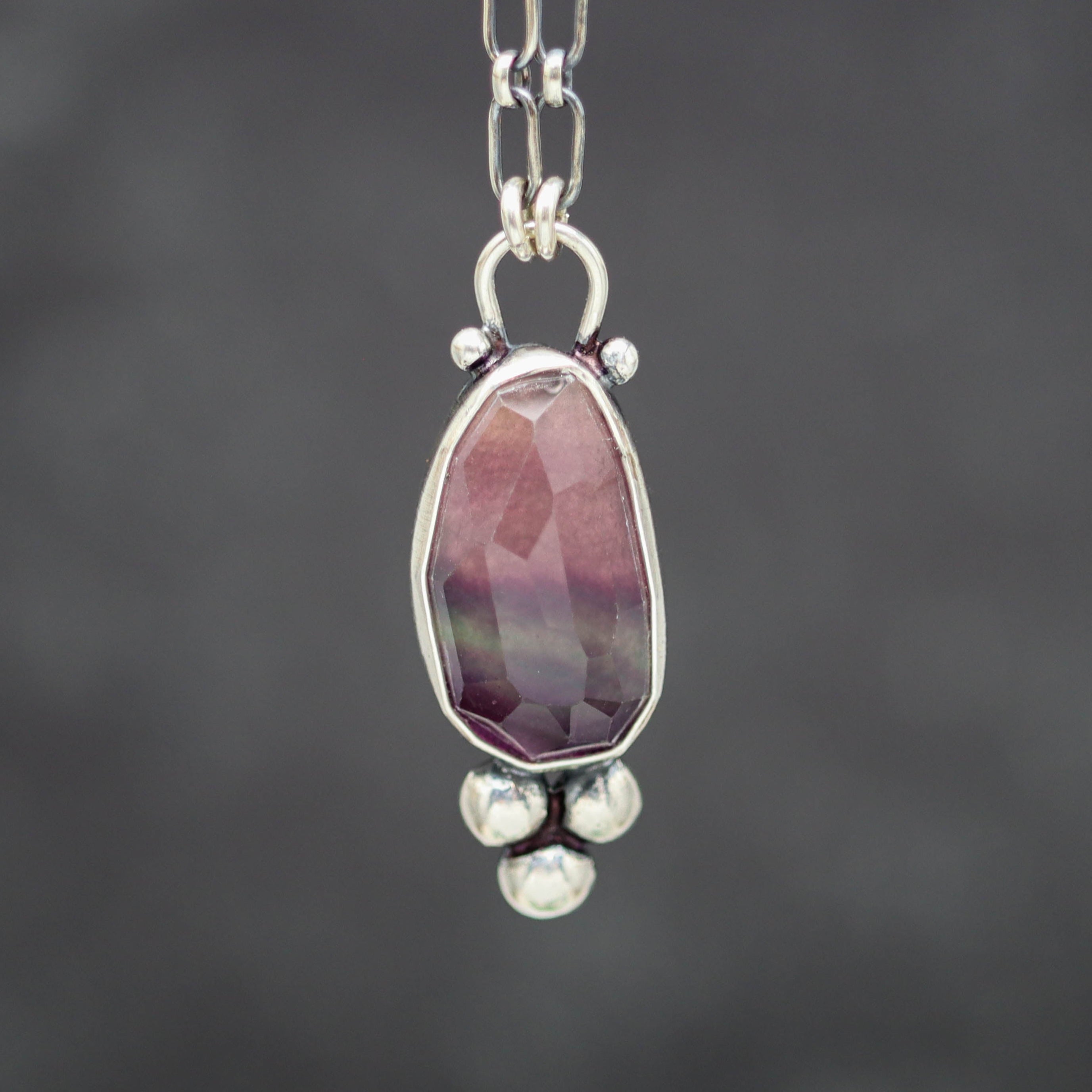 Necklace with a pendant featuring a purple gemstone on a dark background