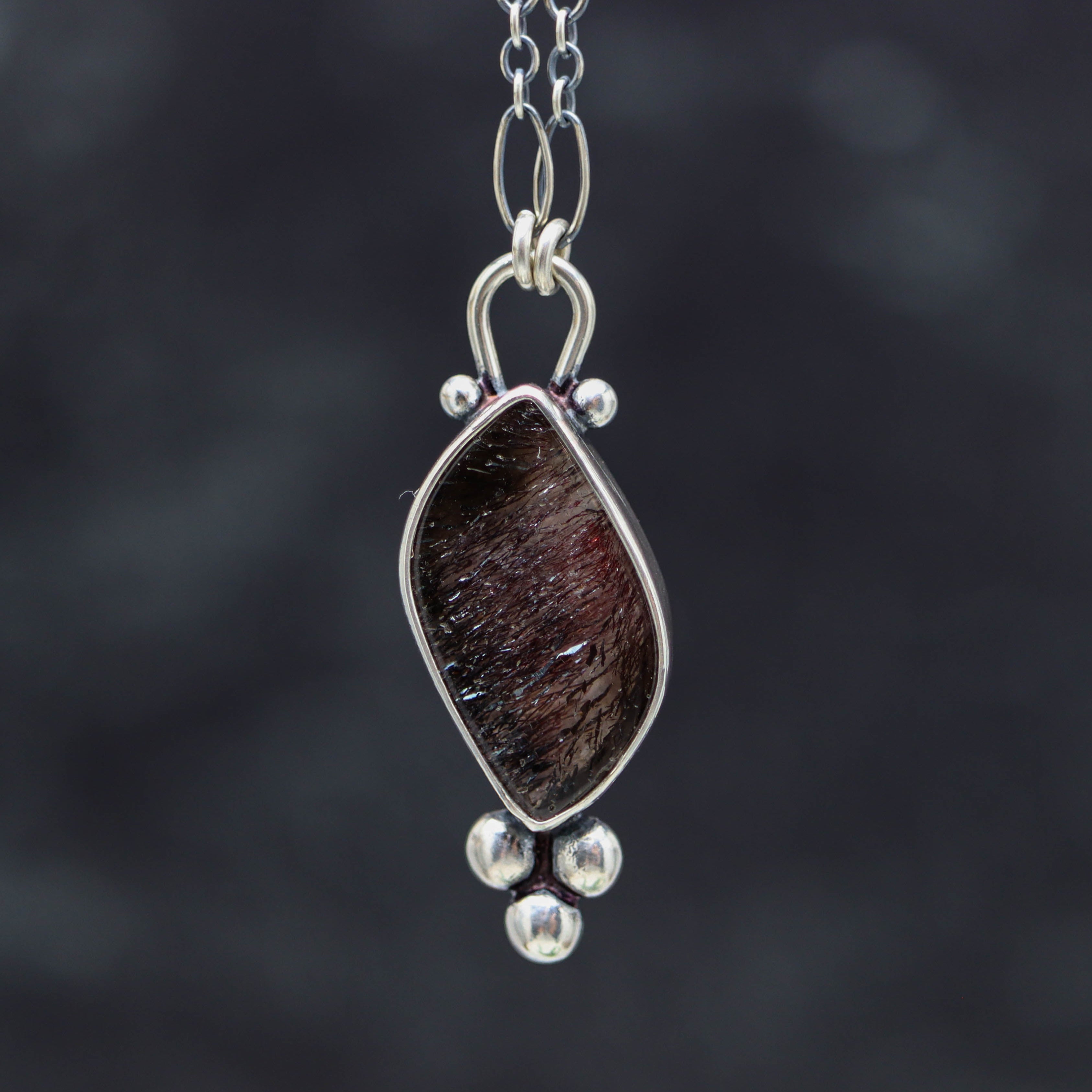 Silver pendant with a dsuper seven stone on a blurred black background 