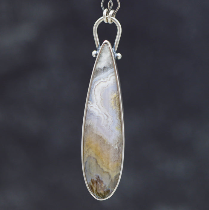 Teardrop-shaped pendant with a patterned stone on a dark background