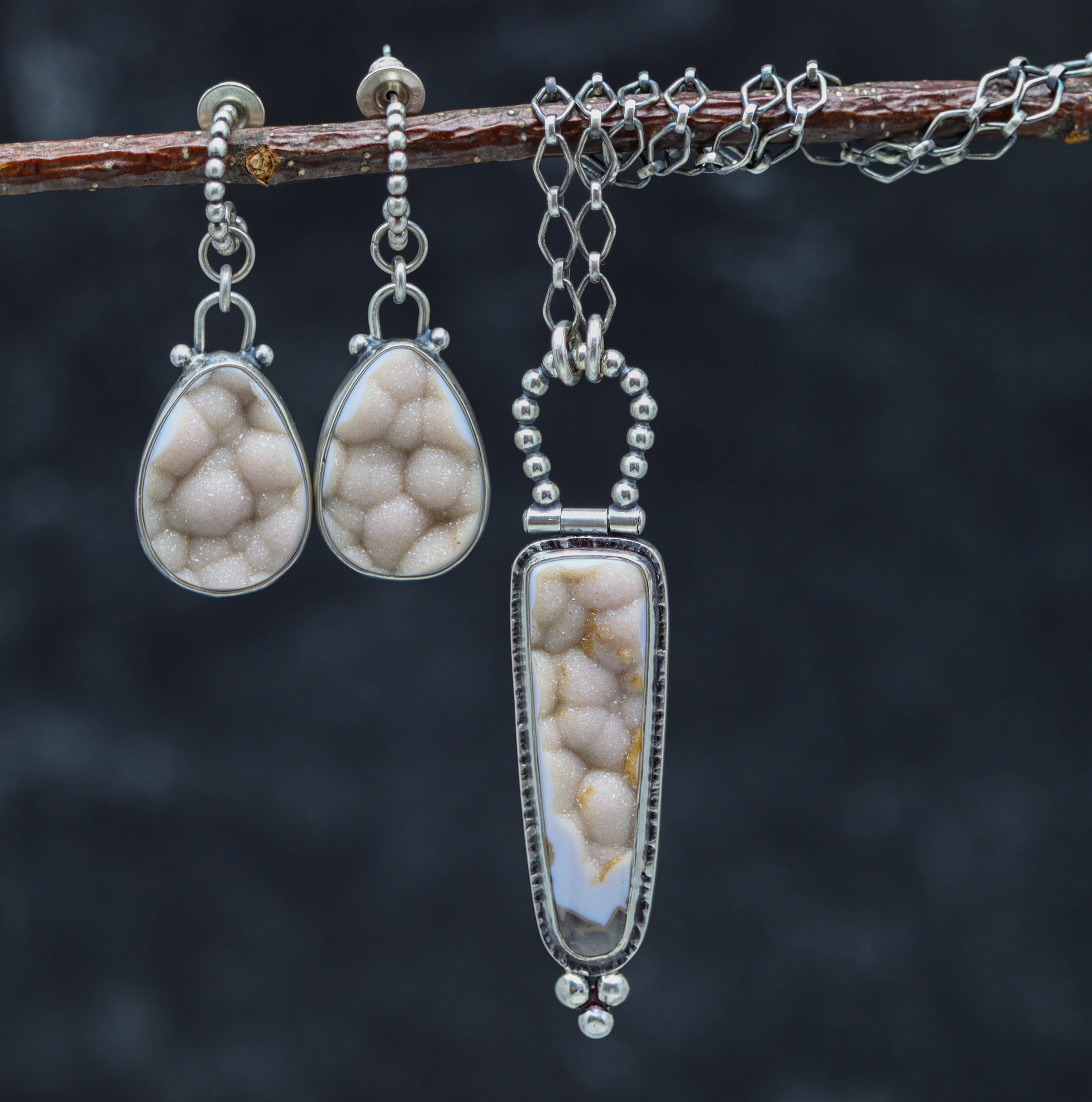 Jewelry set with two earrings and a pendant on a branch against a dark background