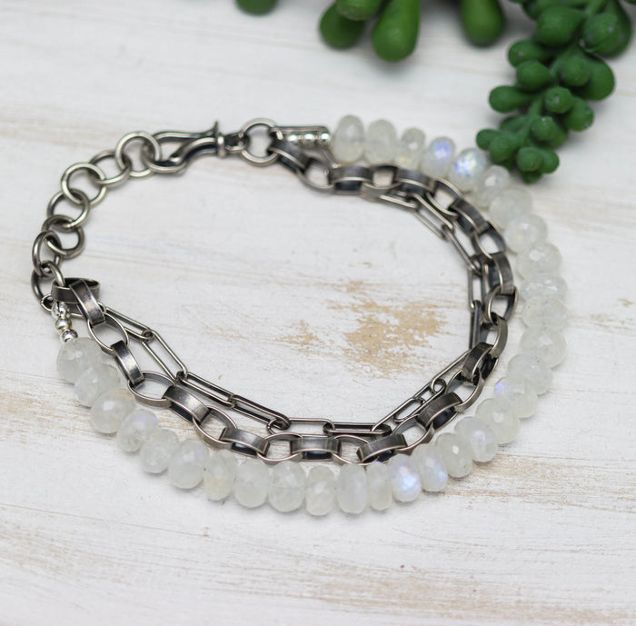 Bracelet with silver chain and beaded design on a light wooden surface with greenery.