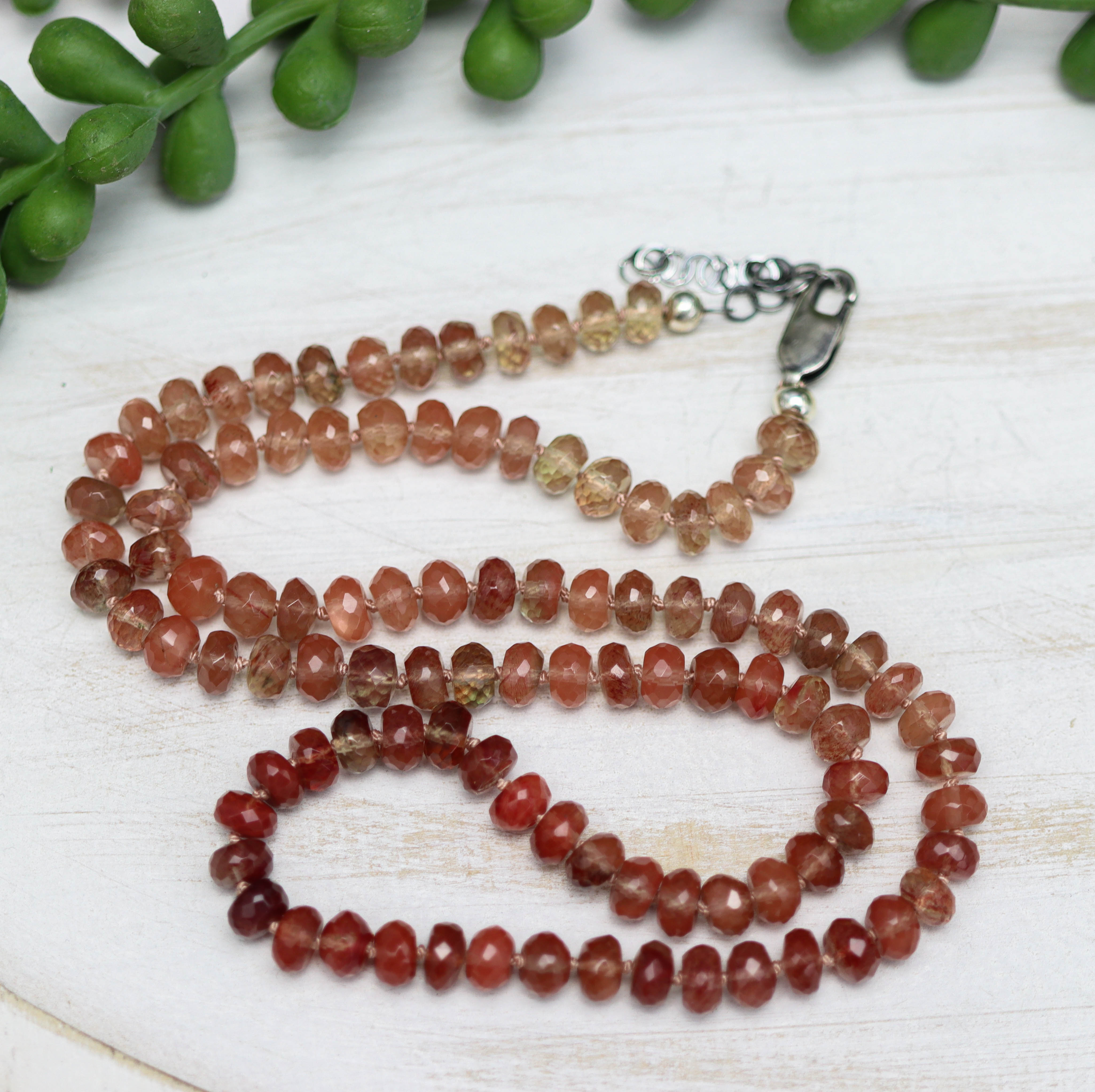 Beaded necklace on a white surface with green leaves in the background