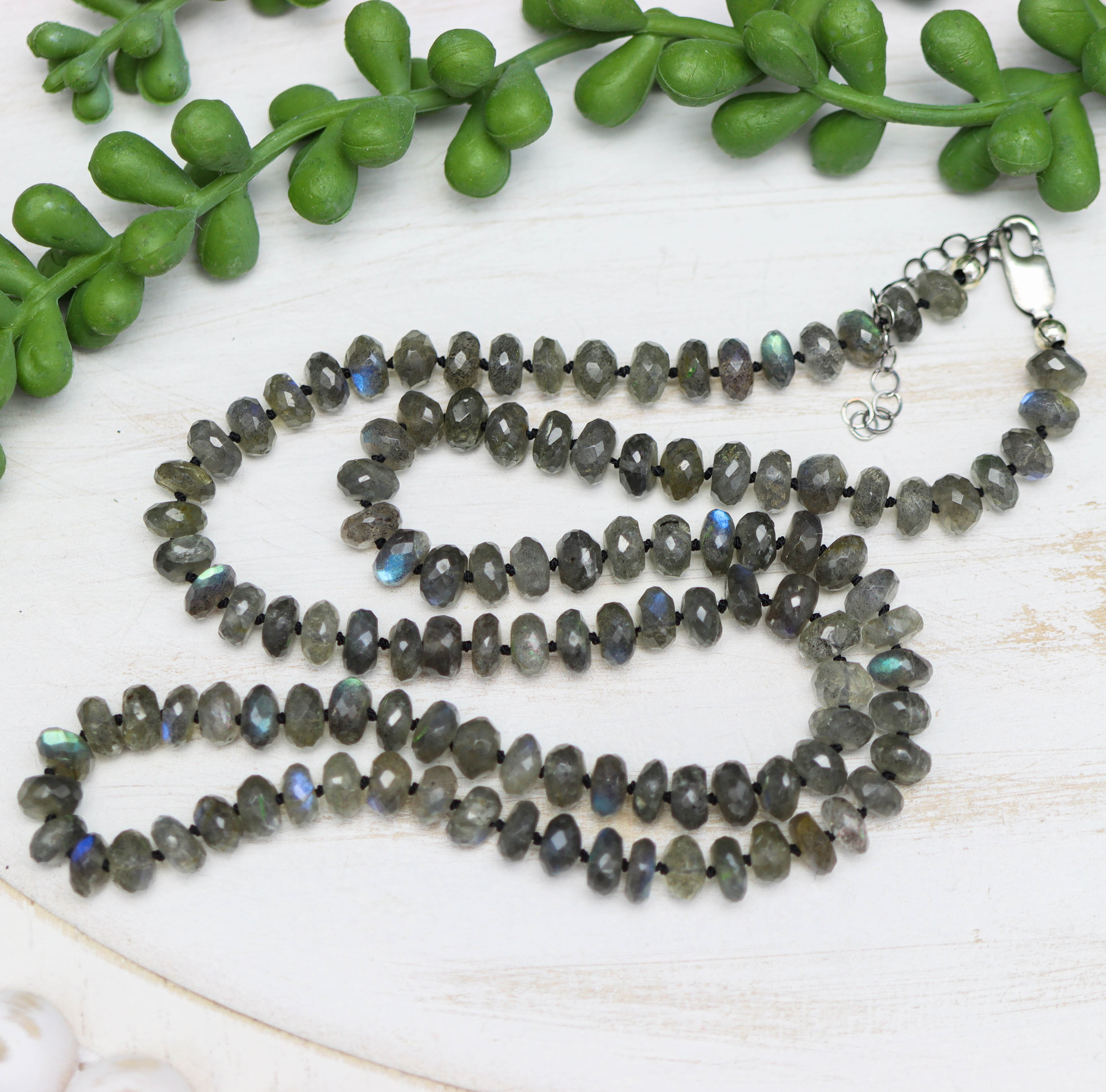 Necklace with Labradorite beads on a white surface with green leaves in the background