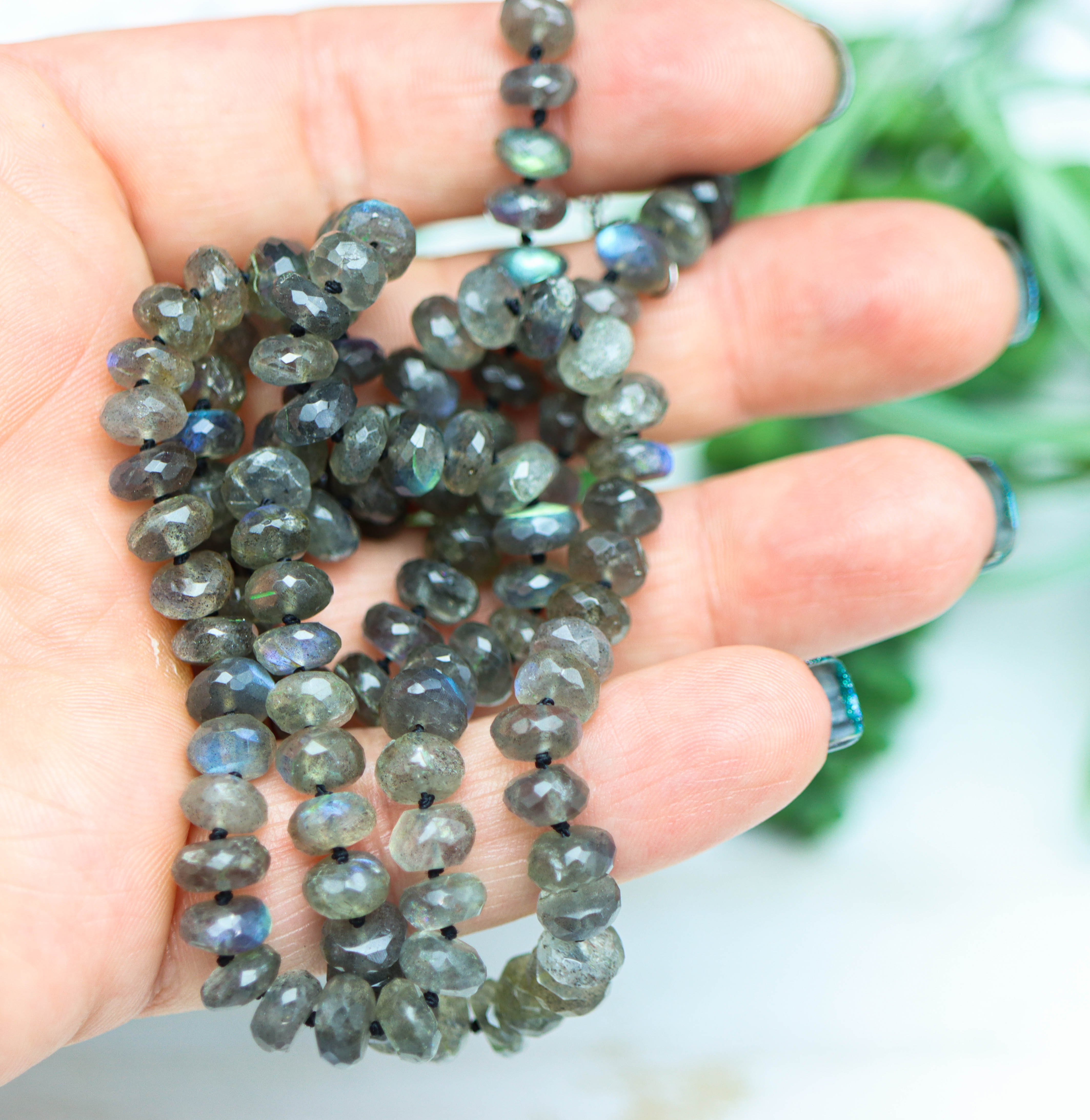 Necklace with Labradorite beads held in a hand against a blurred green background