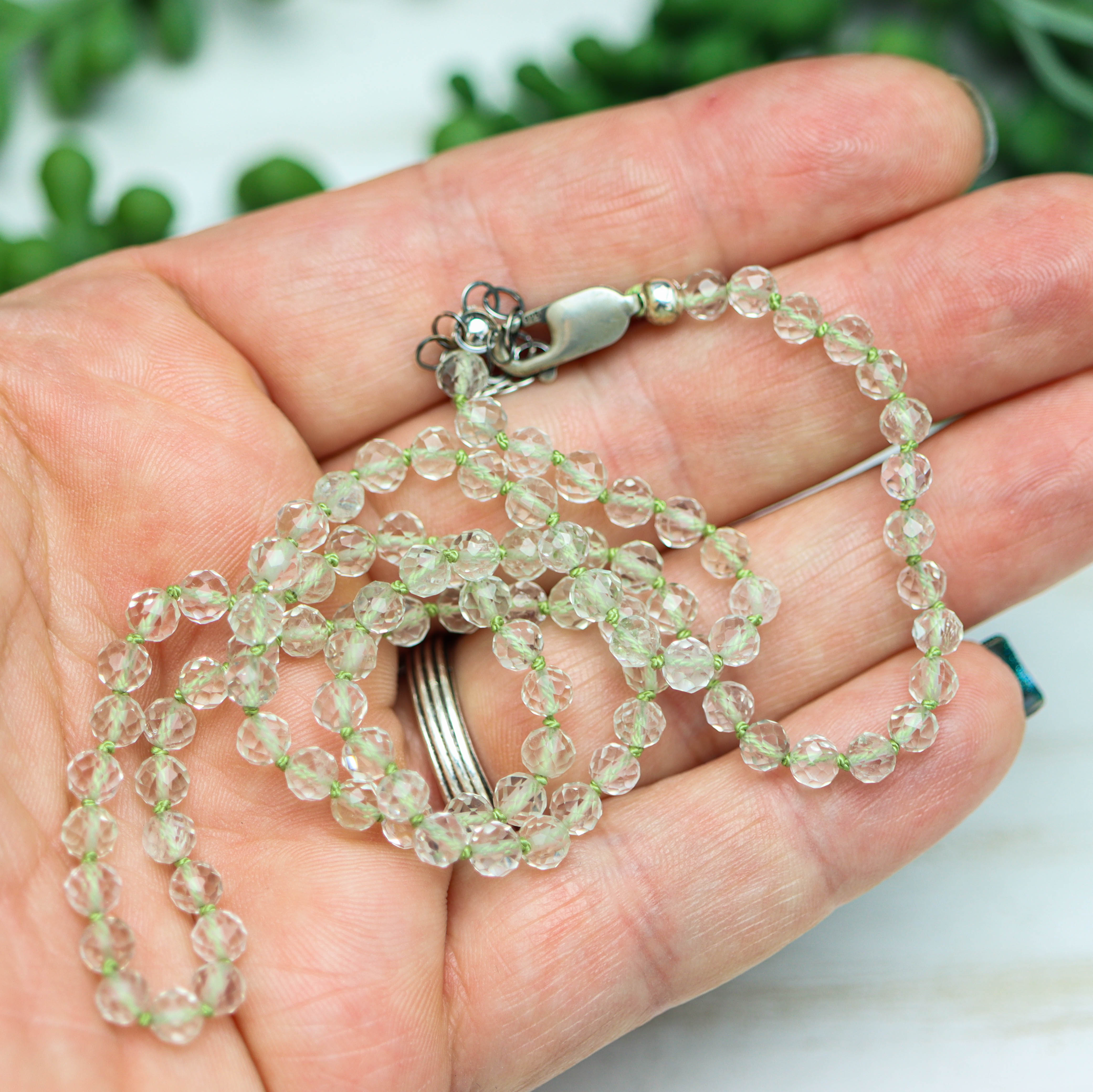 Necklace with clear beads held in a hand against a blurred green background