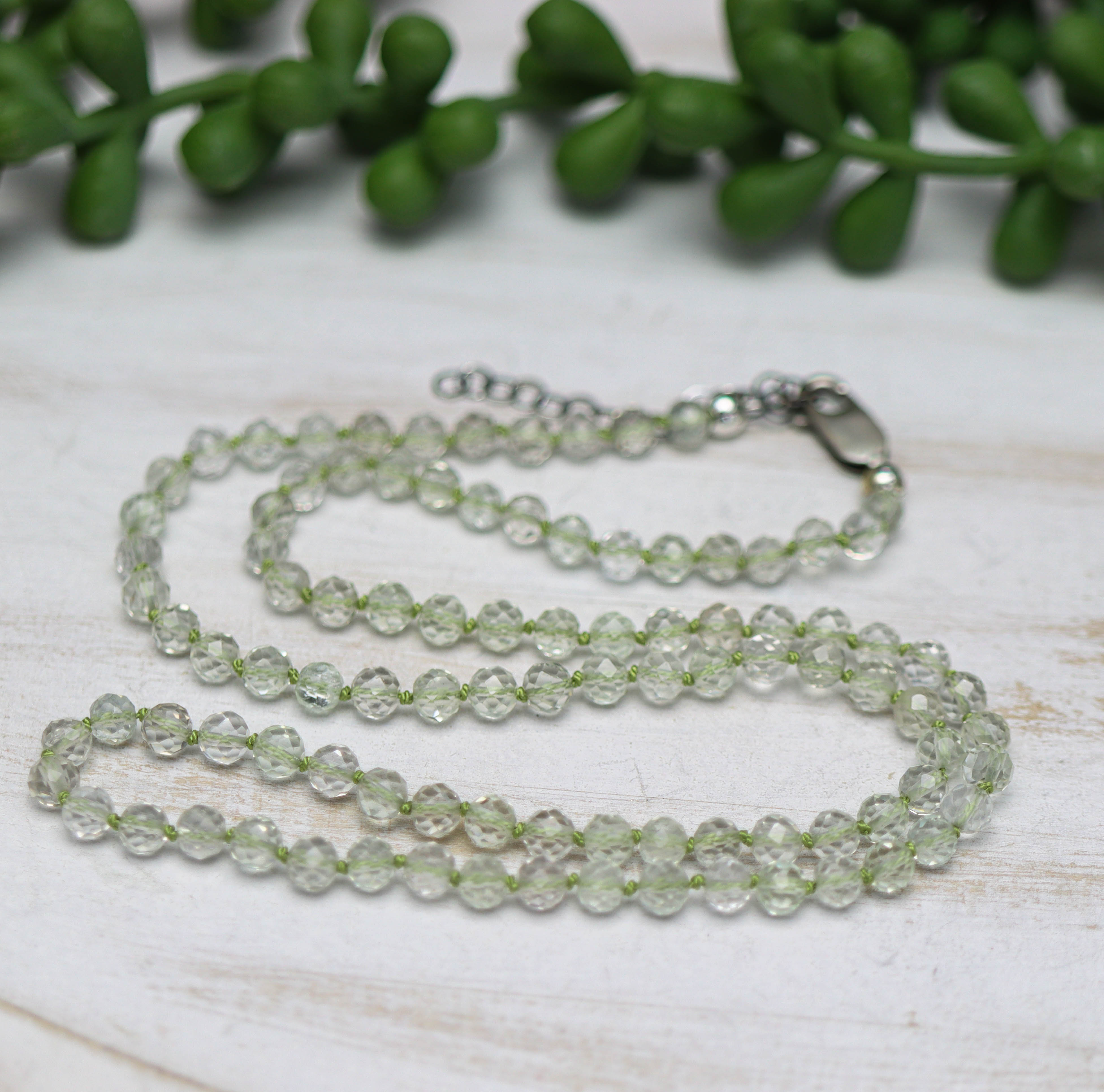 Clear beaded necklace on a light wooden surface with green leaves in the background