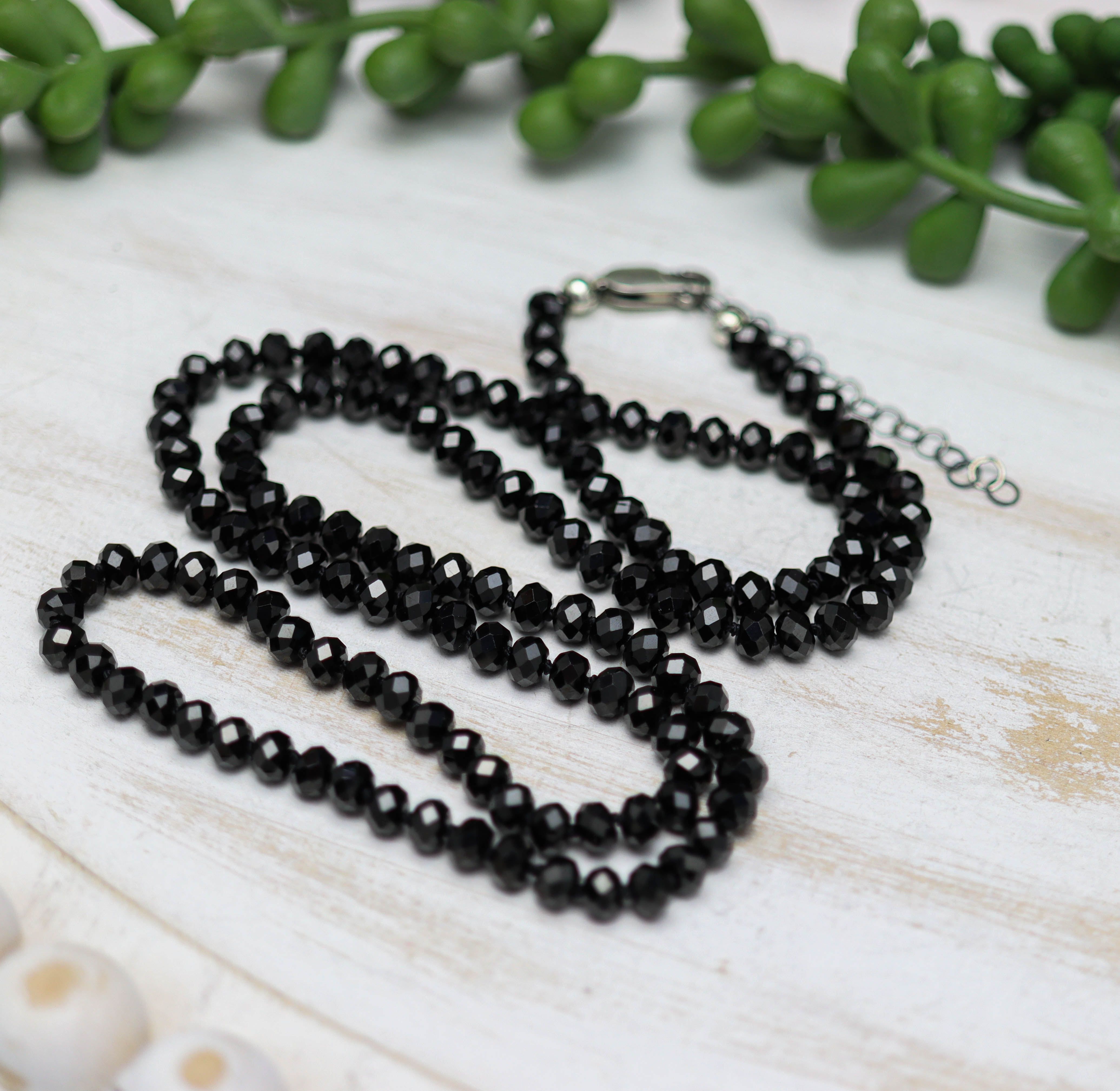 Black beaded necklace on a light wooden surface with green leaves in the background