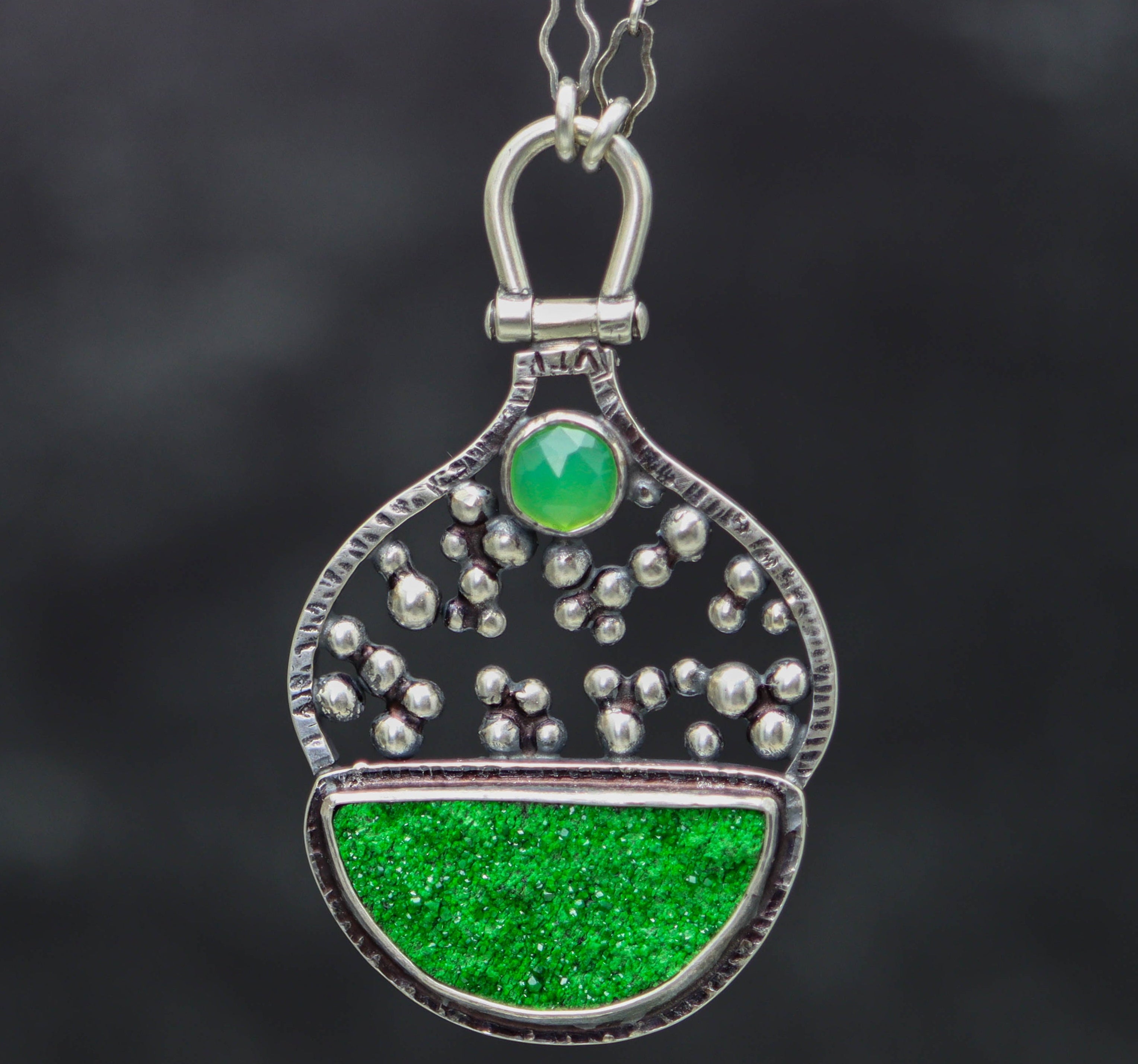 Green pendant necklace with silver accents on a dark background