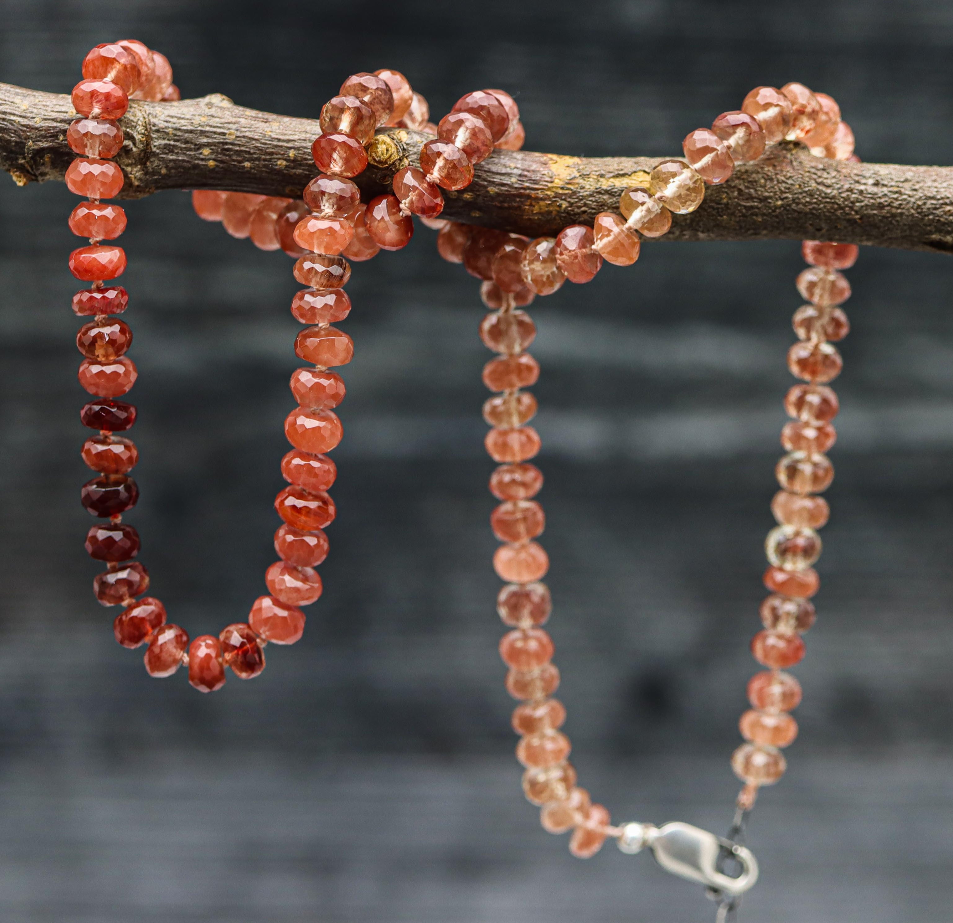 A hand knotted bead necklace with sterling silver closure, featuring faceted andesine beads in shades of red.