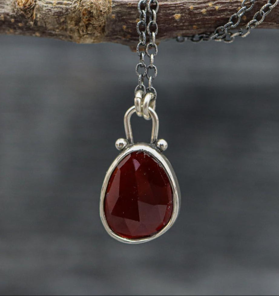 Silver necklace with a red teardrop pendant on a branch against a dark background