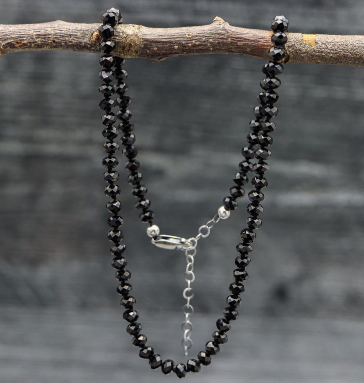 A hand knotted black spinel bead necklace on sterling silver, displayed on a branch, with a lobster claw closure.