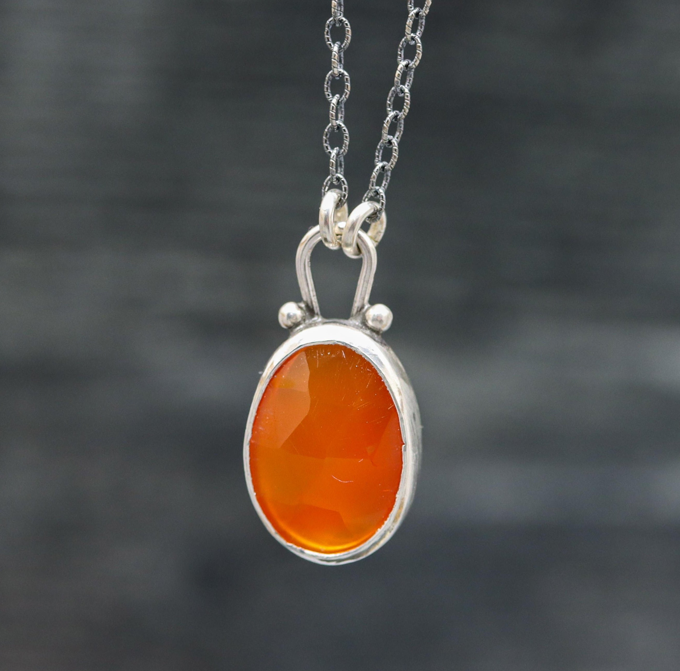 A sterling silver pendant necklace with a juicy bright orange carnelian gemstone in a faceted rose cut, silver ball accents, and a silver cable link chain.