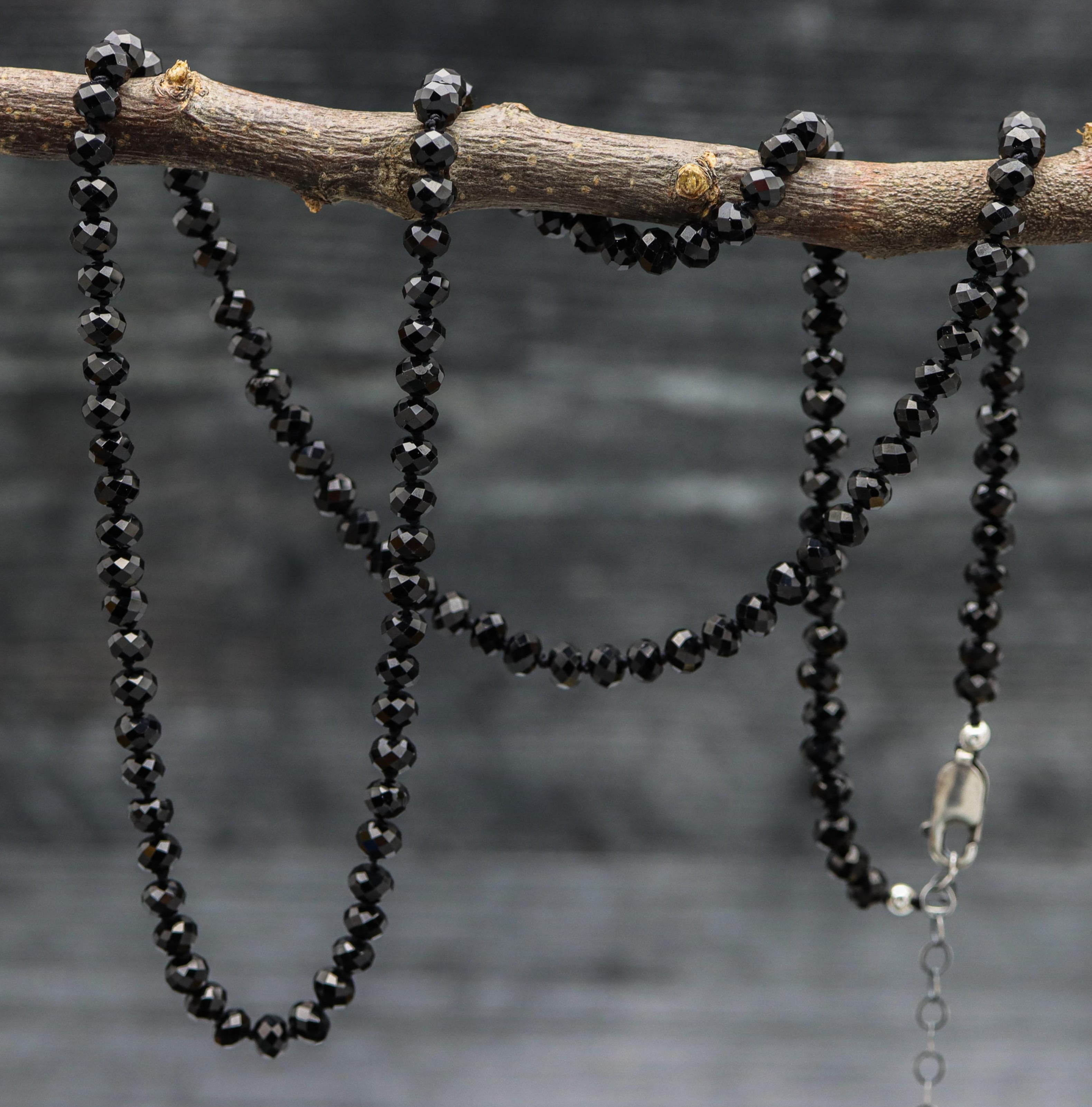 A hand knotted black spinel beaded necklace made of sterling silver and black spinel stones, displayed on a branch.