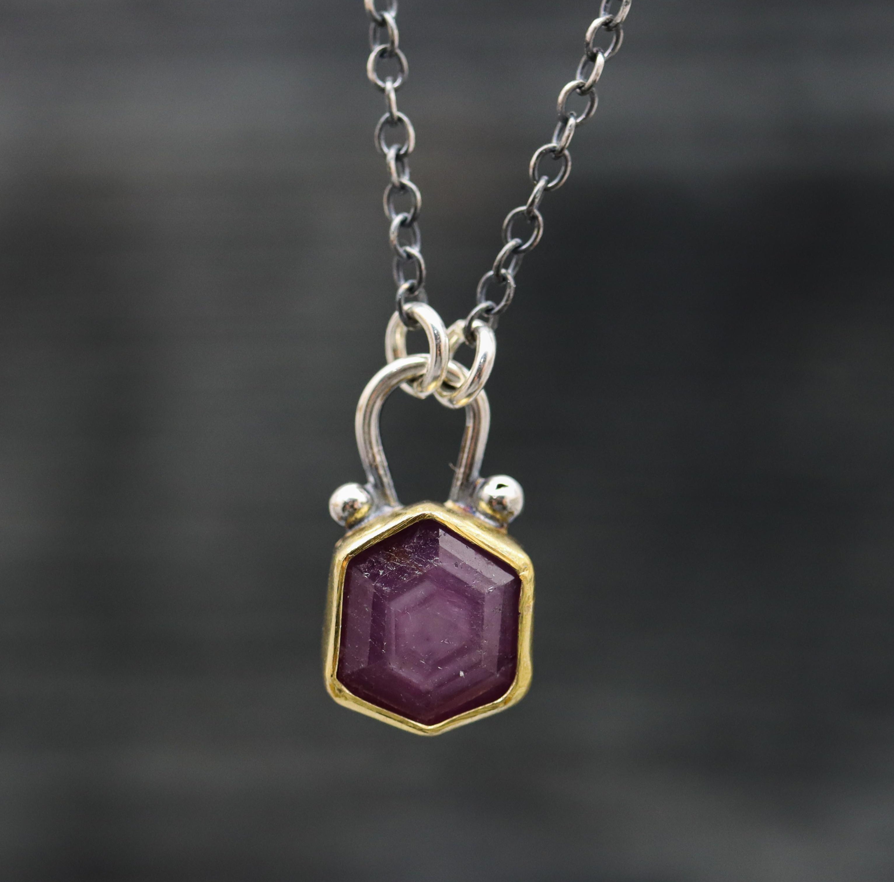 A ruby pendant necklace with a 22k gold bezel, displayed on a sterling silver chain.