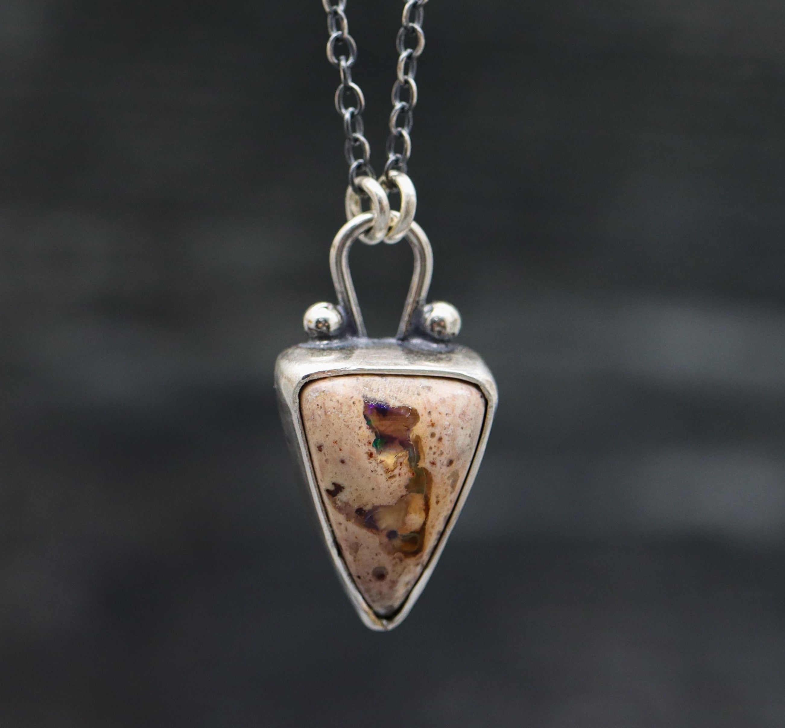 A sterling silver pendant necklace with a Mexican fire opal centerpiece and small silver ball accents, displayed against a dark background.