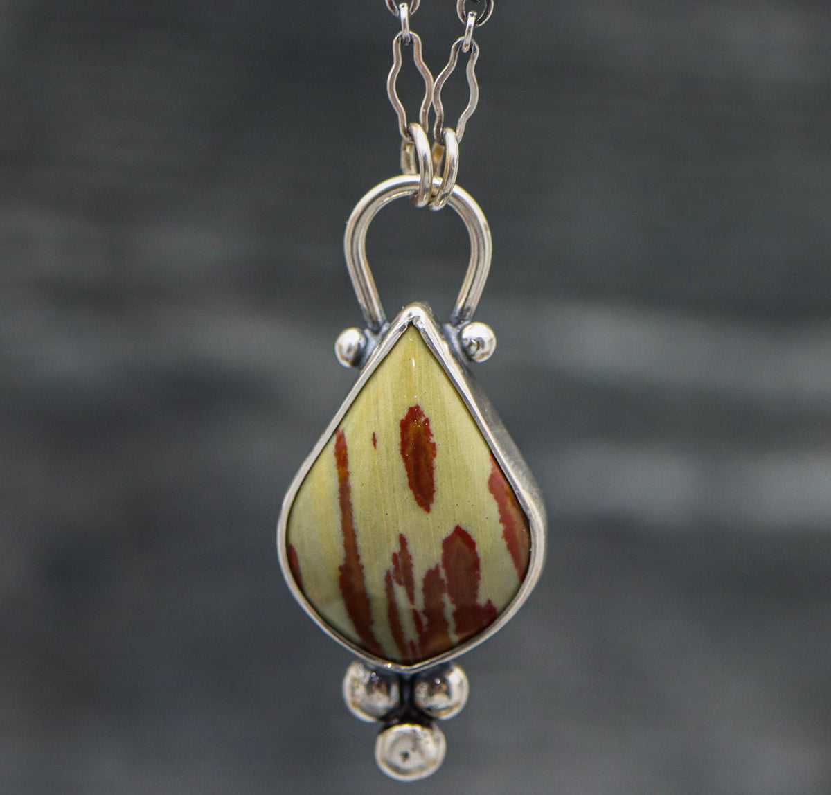 A sterling silver pendant featuring an owyhee jasper gemstone with a textured metal surface mimicking the stone's pattern, displayed on a silver chain.