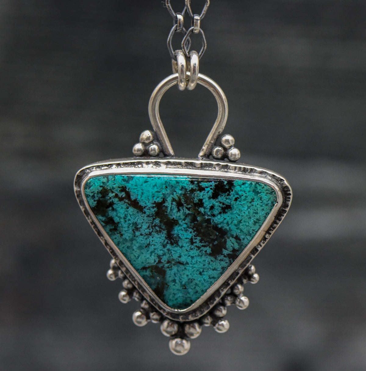 A sterling silver pendant featuring a turquoise blue chrysocolla gemstone with black speckles, set in a sterling silver bezel, attached to a diamond link chain with a lobster claw clasp.